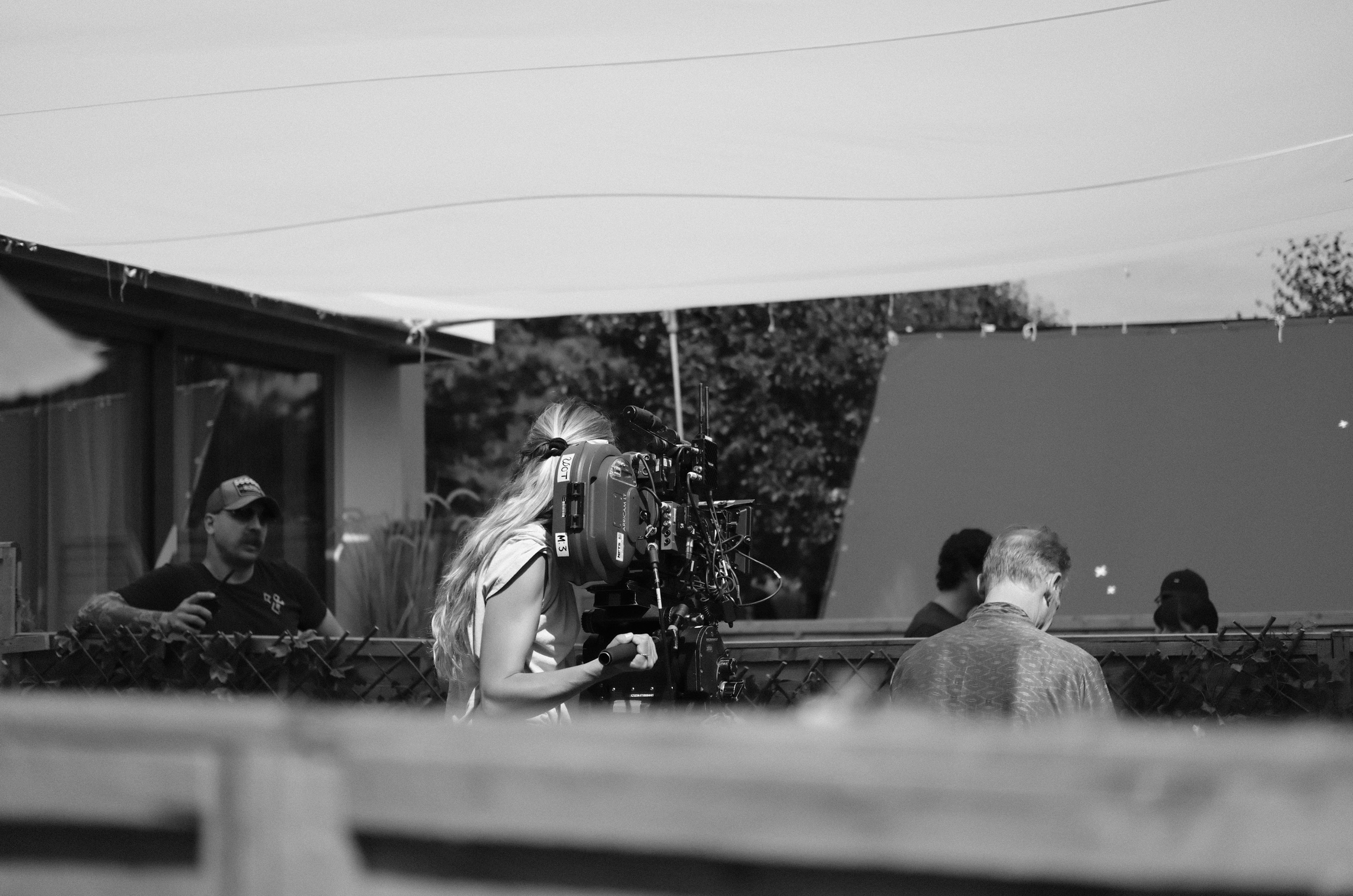 A woman operating a professional video camera outdoors with several people in the background.