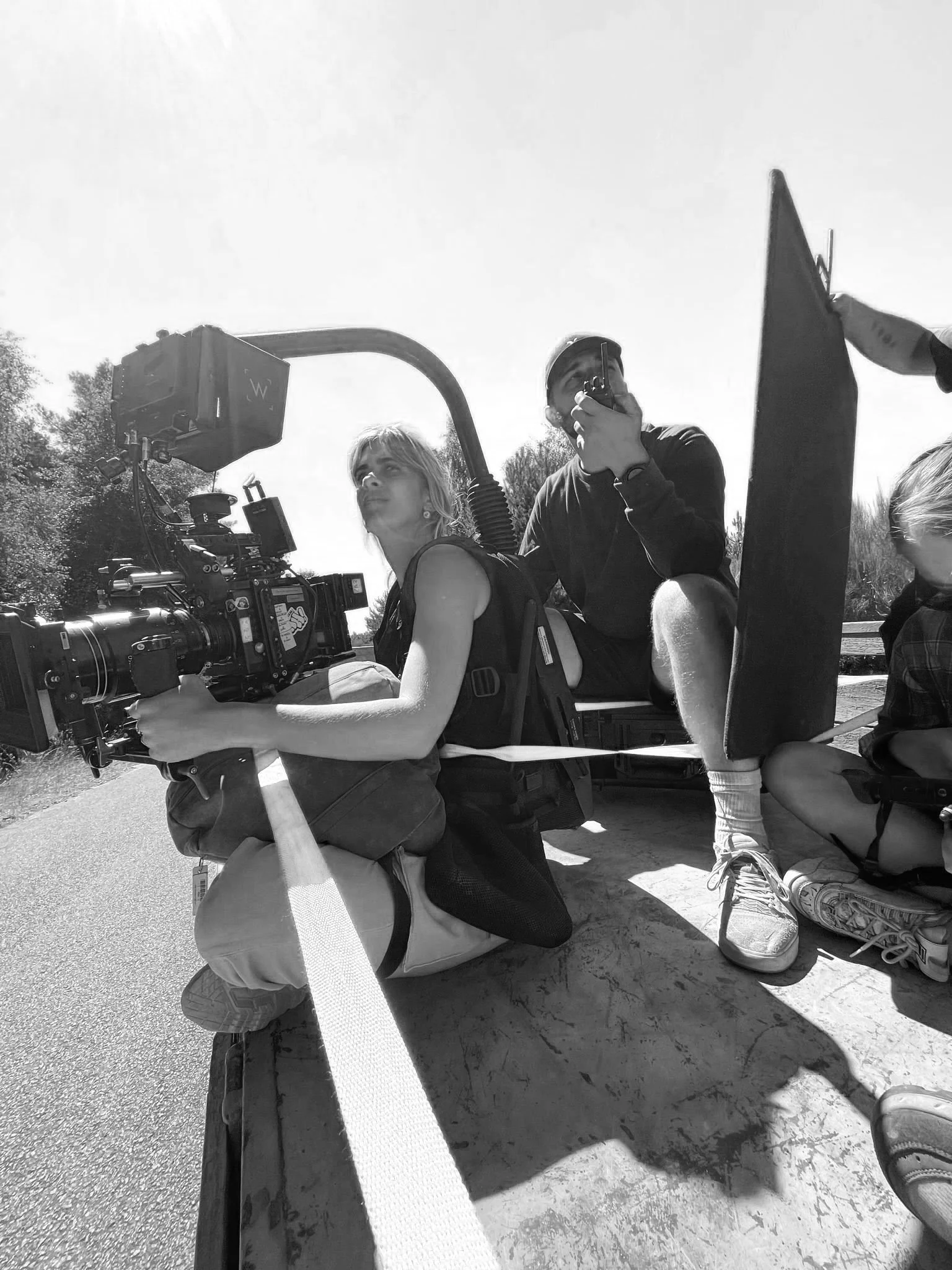 A crew of two filming a scene outdoors during the day, with a camera mounted on a dolly, and a person holding a walkie-talkie.