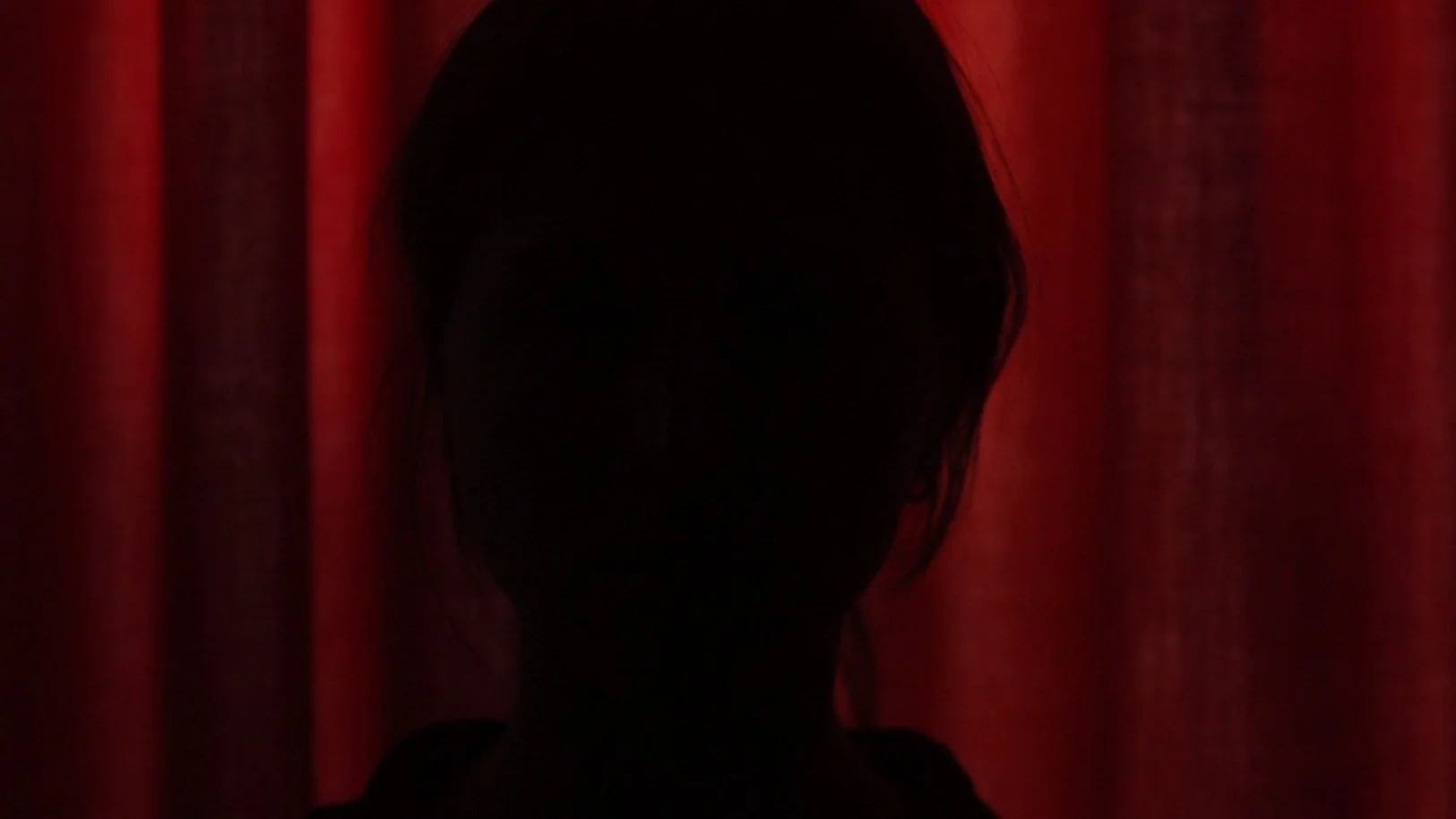 Silhouette of a person with short hair standing in front of red curtains.
