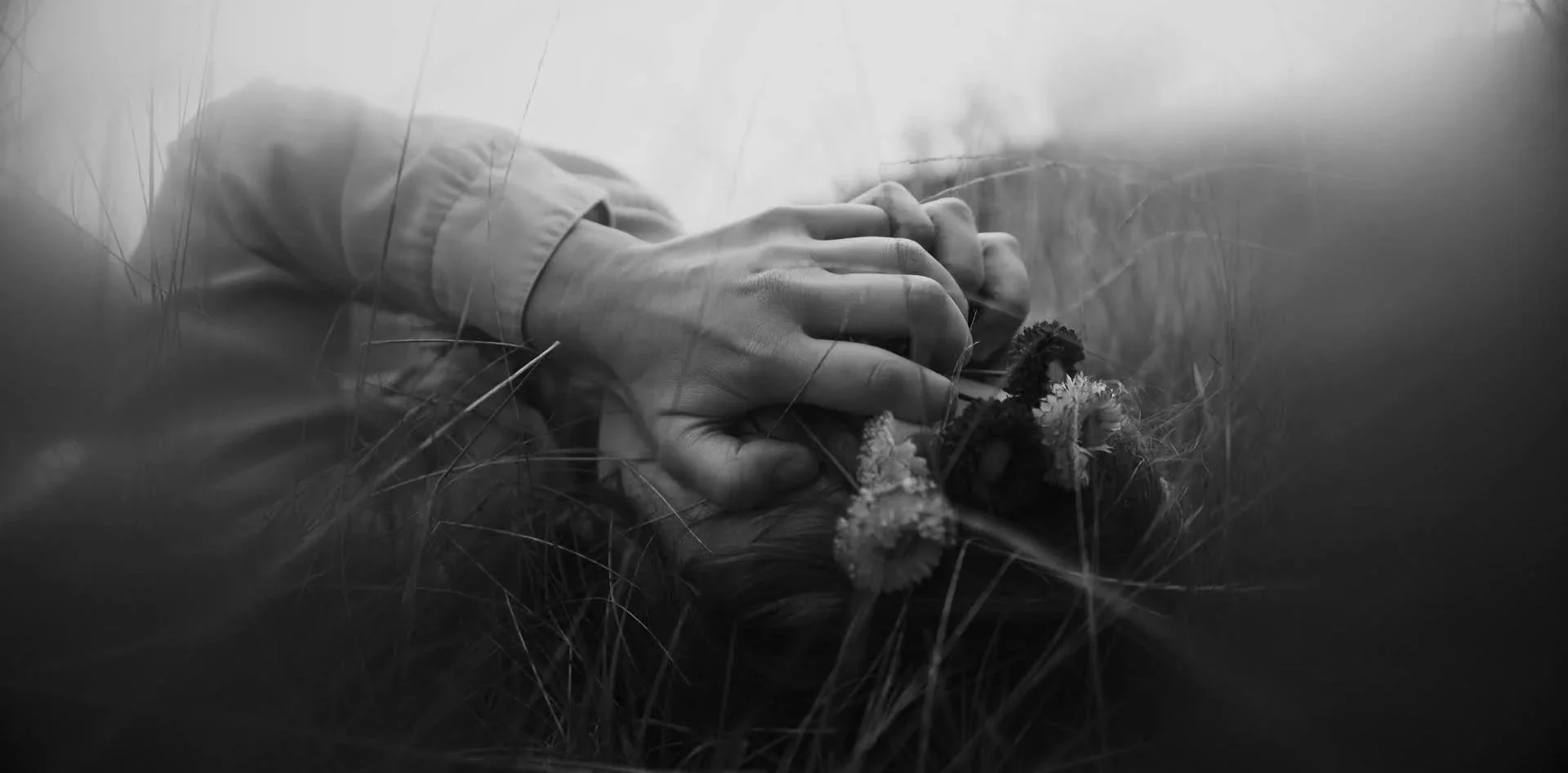 Black and white photo of a hand holding a small bouquet of flowers, lying on grass.