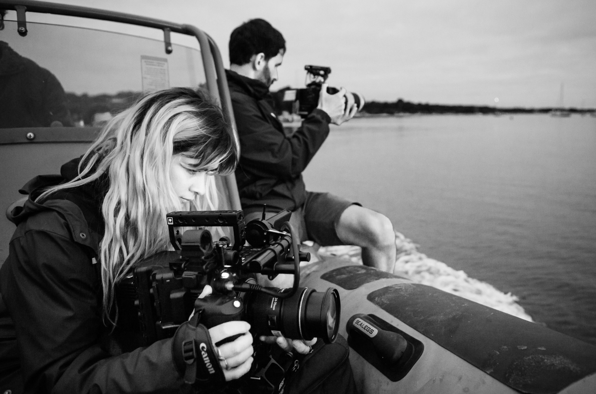 Two videographers on a boat photographing the water at dusk