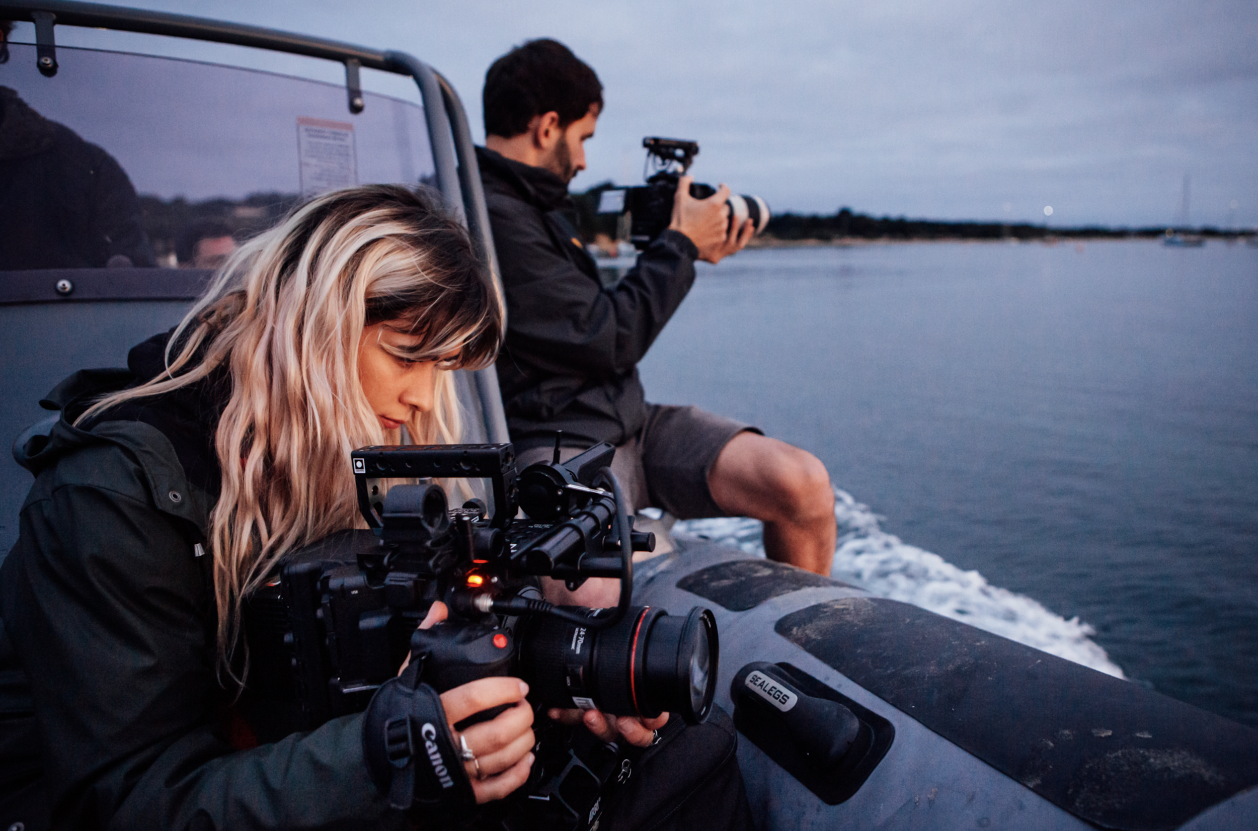 Two videographers on a boat photographing the water at dusk