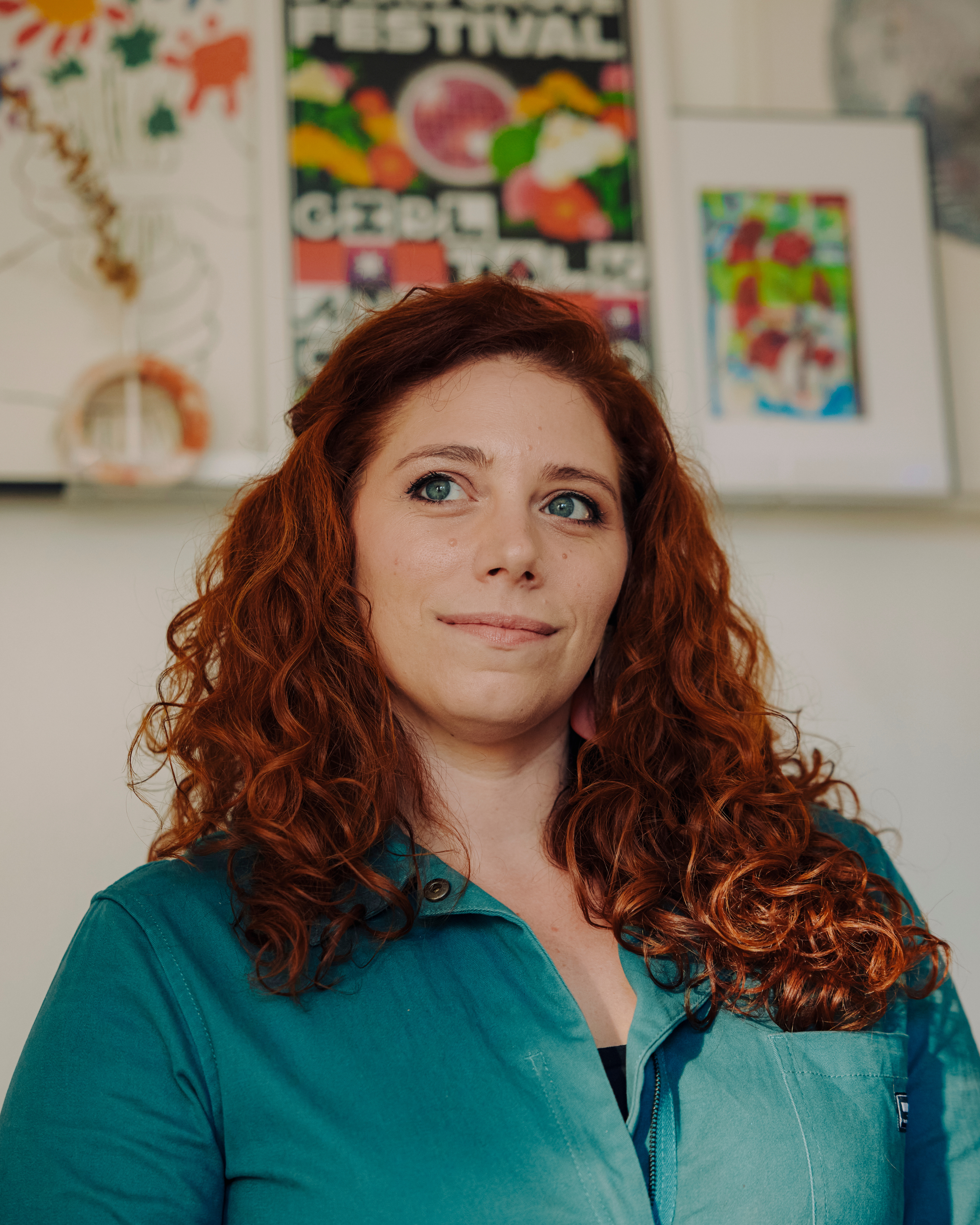 Liz Morrison, strategic story coach, smiling in a teal jumpsuit in front of colorful posters