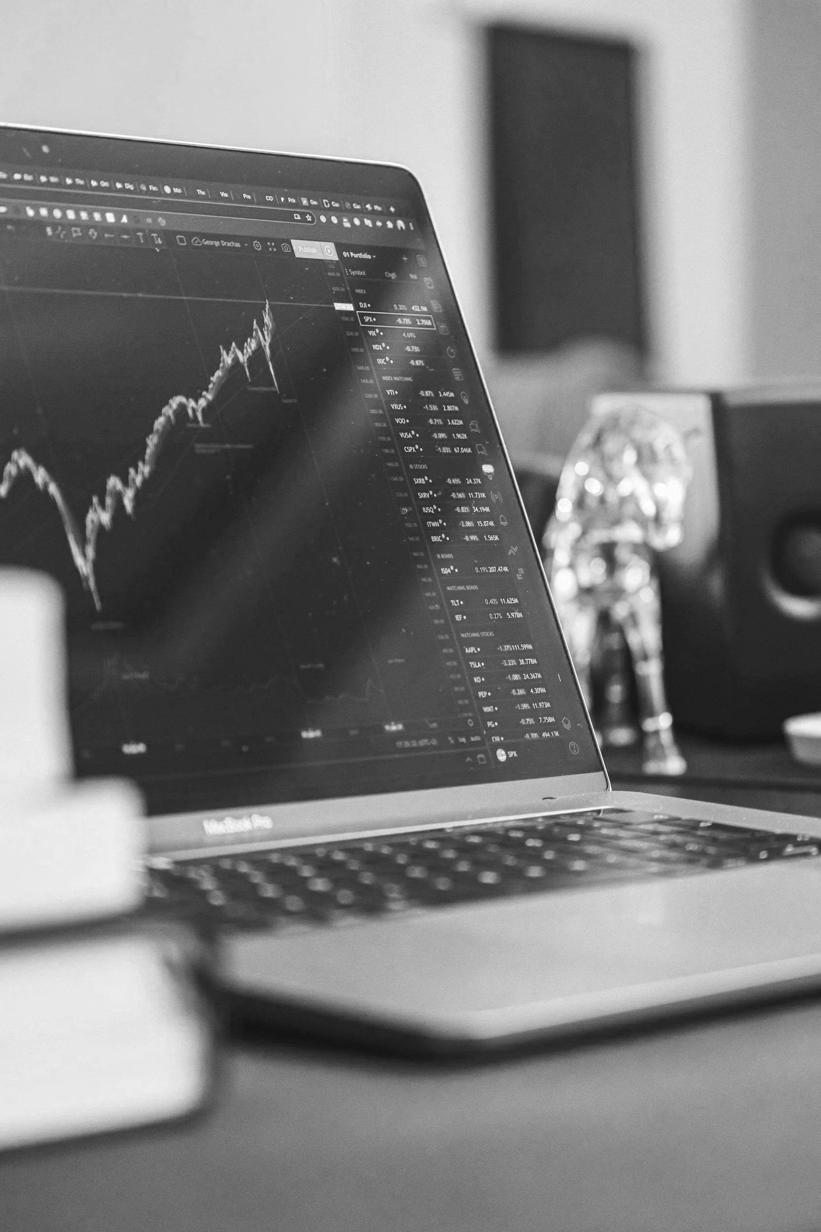Black and white photo of a laptop displaying stock market chart and data, with a blurred background.