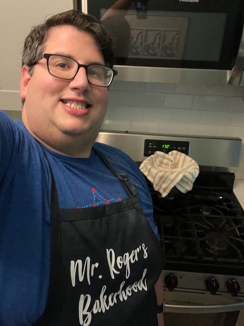 Miles Roger wearing "Mr. Roger's Bakerhood" apron in front of oven.
