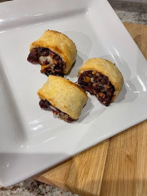 Three orange-cranberry filled rugelach on a white square plate.