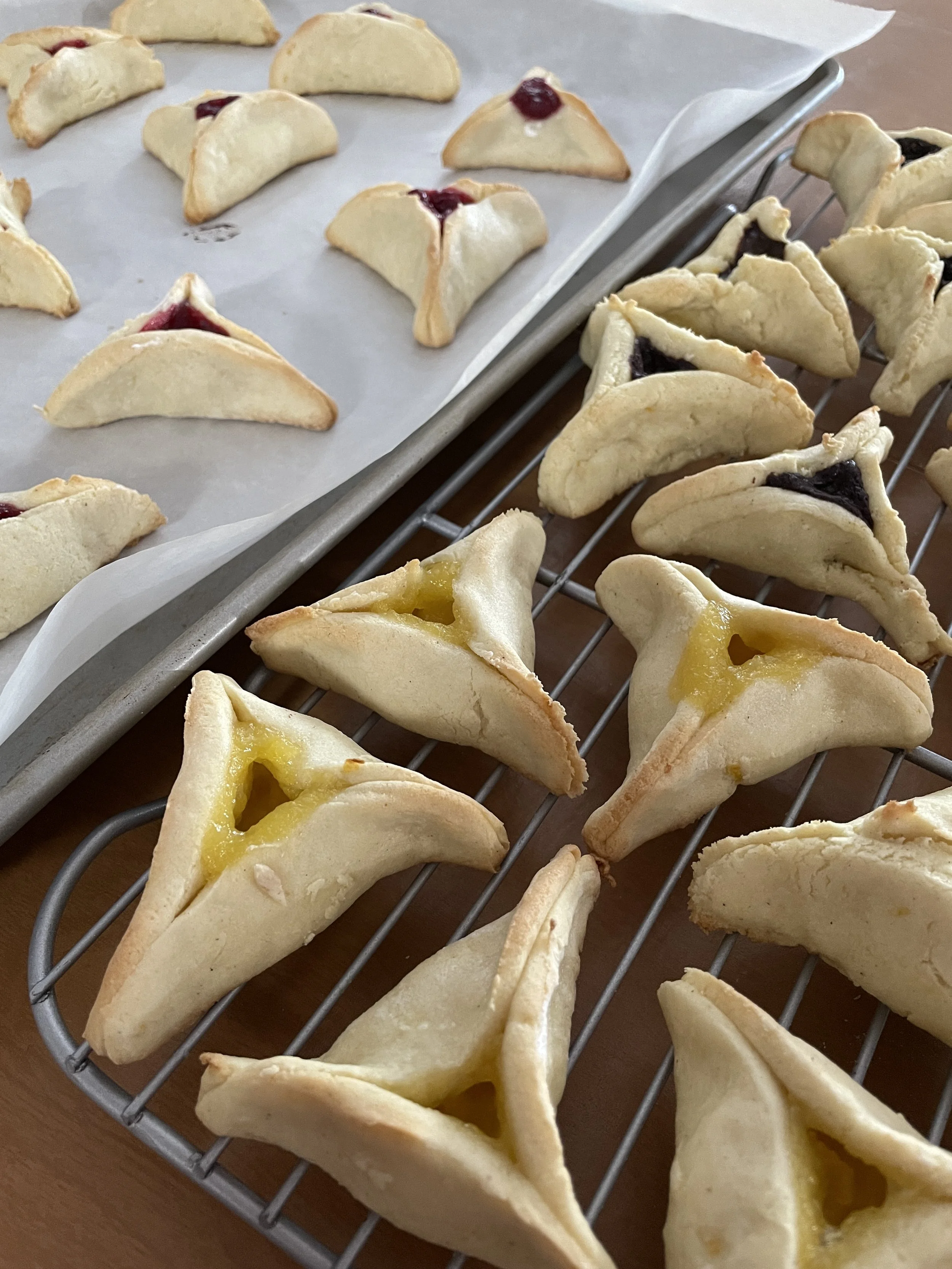 Hamentashen on a baking sheet and cooling rack.