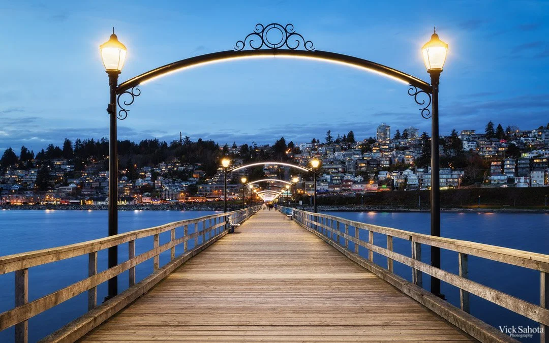 The White Rock pier and waterfront at dusk, with the hillside homes lit above the bay.
