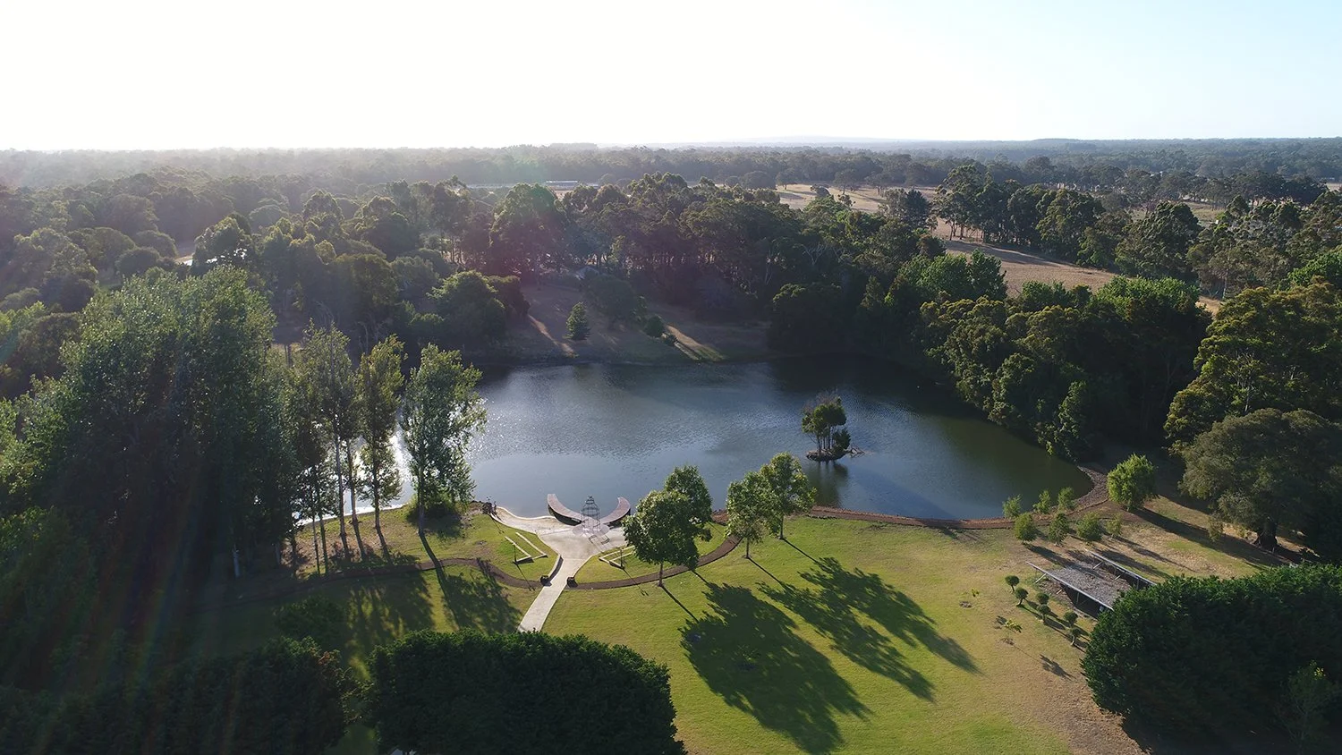 Aerial view of Losari Retreat with a pond, lush green trees, walking paths, and benches during daytime.