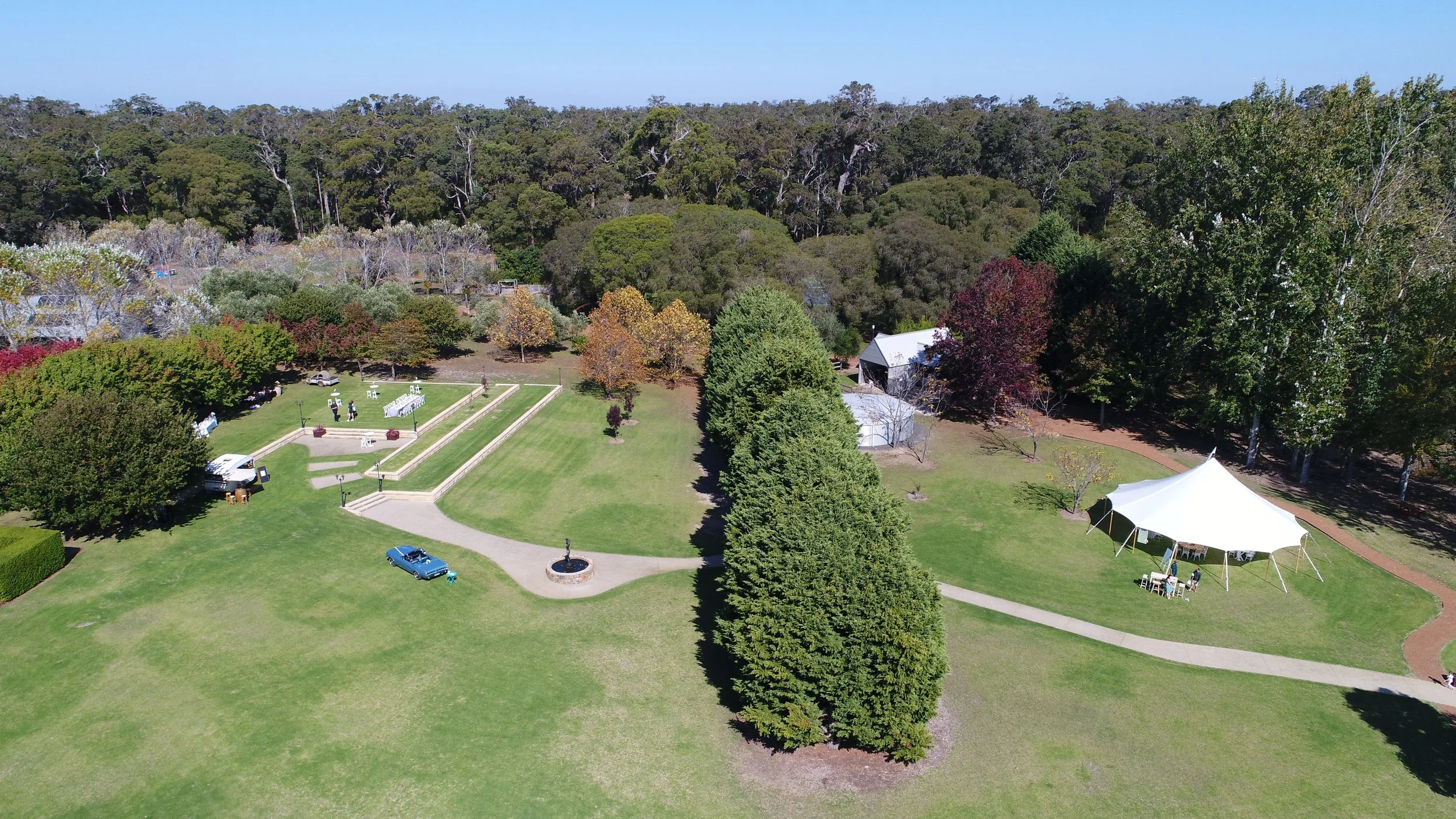 Aerial view of Losari Retreat with green grass, trees, a small stage, a tent, and a paved walkway.