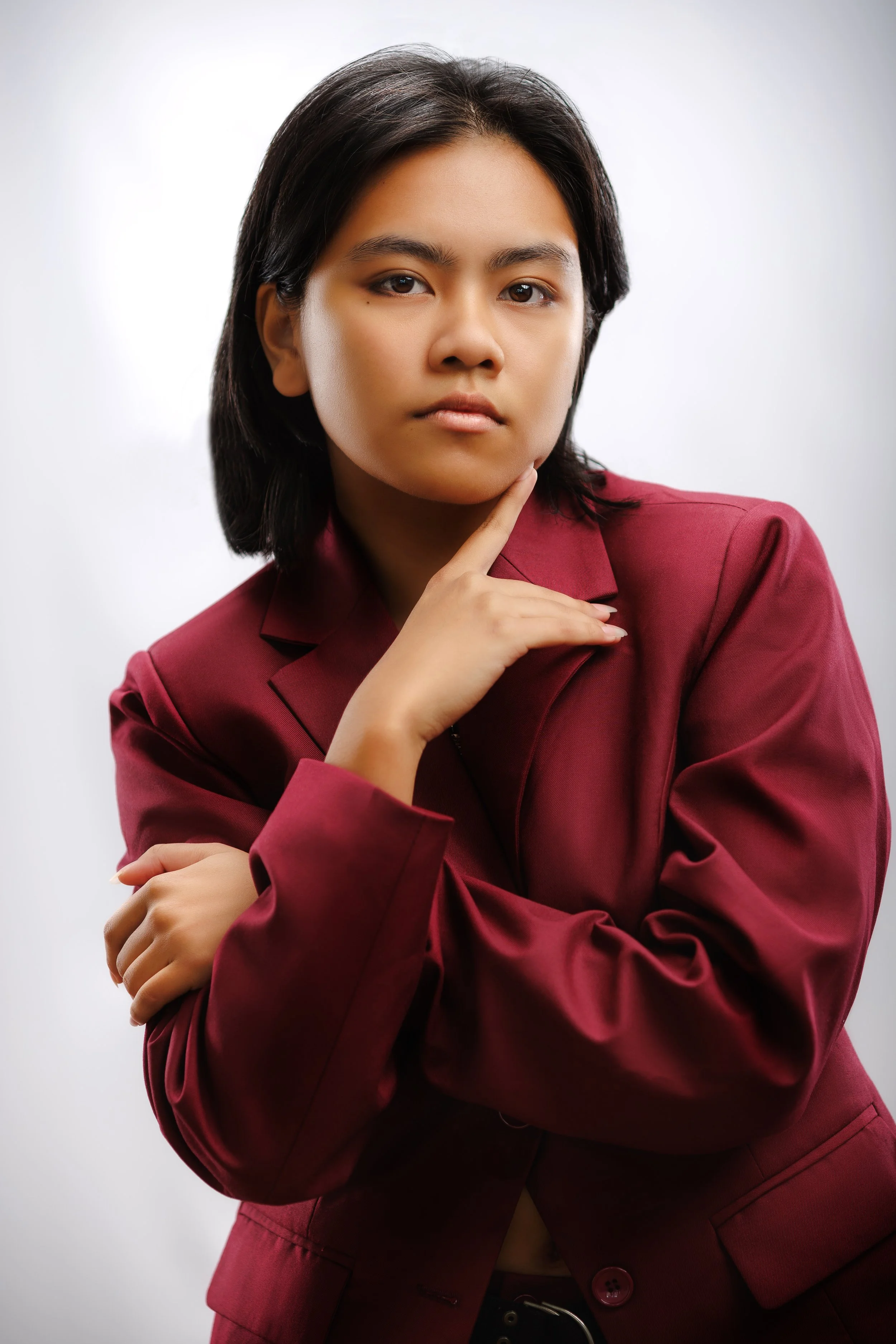 Portrait of a woman with short black hair wearing a maroon blazer, posing thoughtfully against a neutral background.