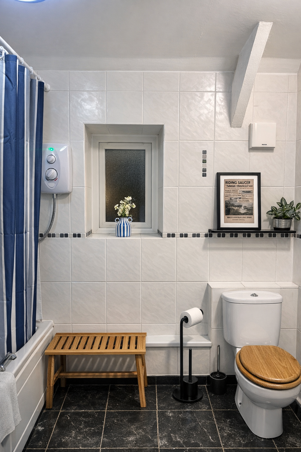 Modern bathroom with white tiled walls, black tiled floor, wooden toilet seat, small window with a blue and white vase of flowers, framed picture, potted plant, shower with a blue striped curtain, wooden bench, and toilet paper holder.