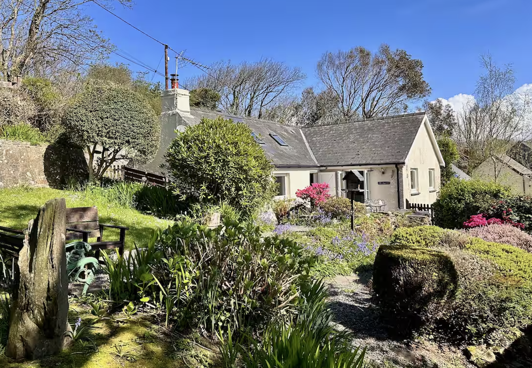 A charming house with a garden surrounded by lush greenery, blooming flowers, and a blue sky.