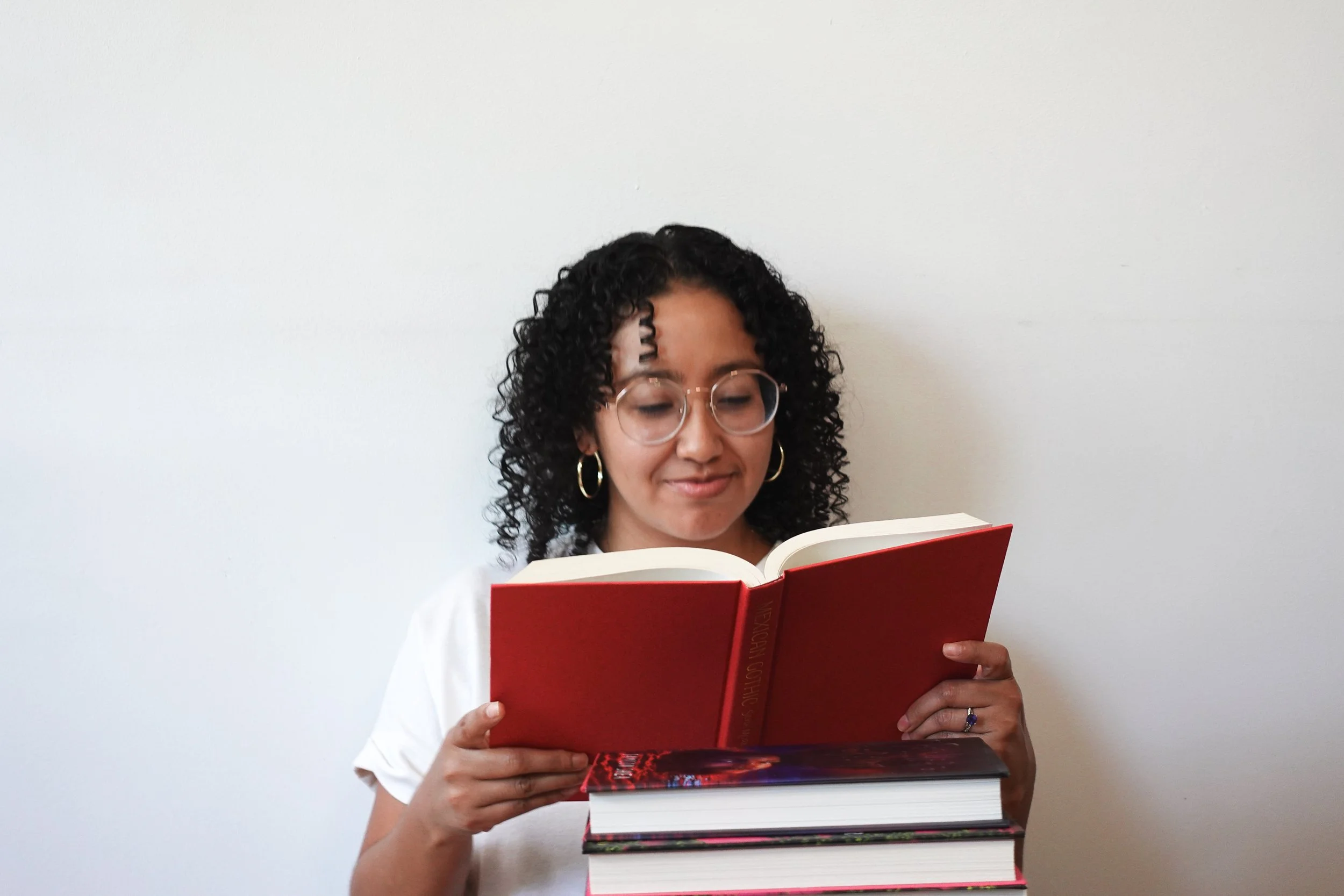 Book coach Sabrina reads a hardcover copy of Mexican Gothic without the dust jacket behind a pile of books.