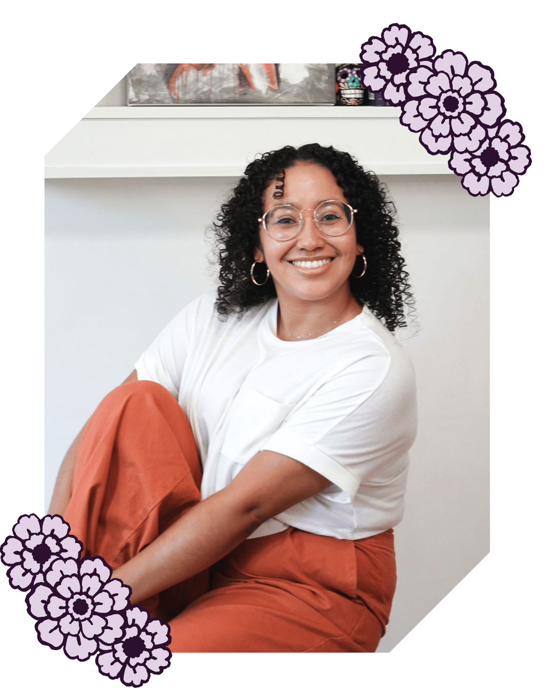Book Coach Sabrina sits on a stool with one foot up on the stool and her arms wrapped around her leg. She smiles at the camera.
