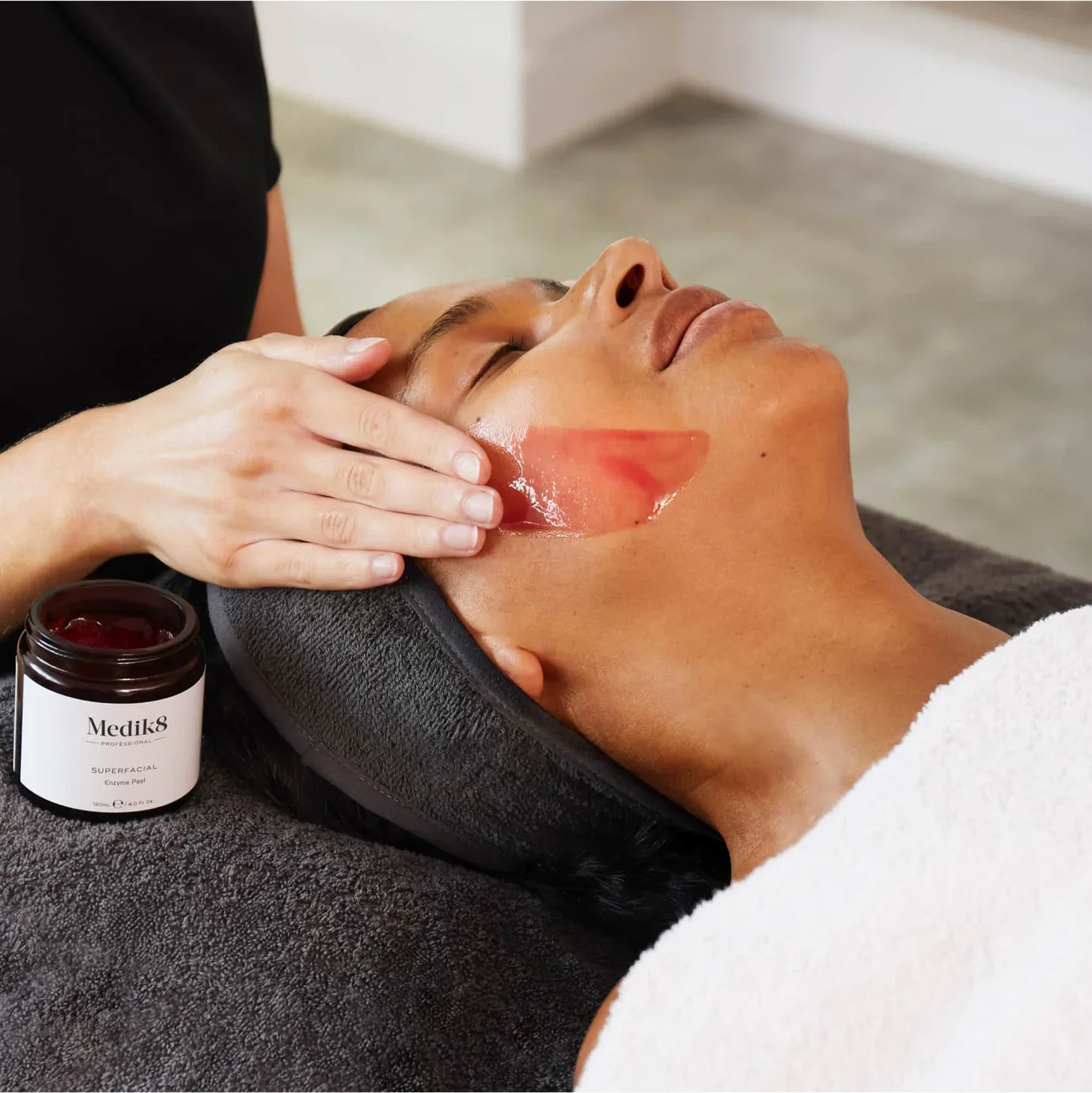 A woman lying on a treatment table with a facial mask, relaxing in a spa or wellness center.