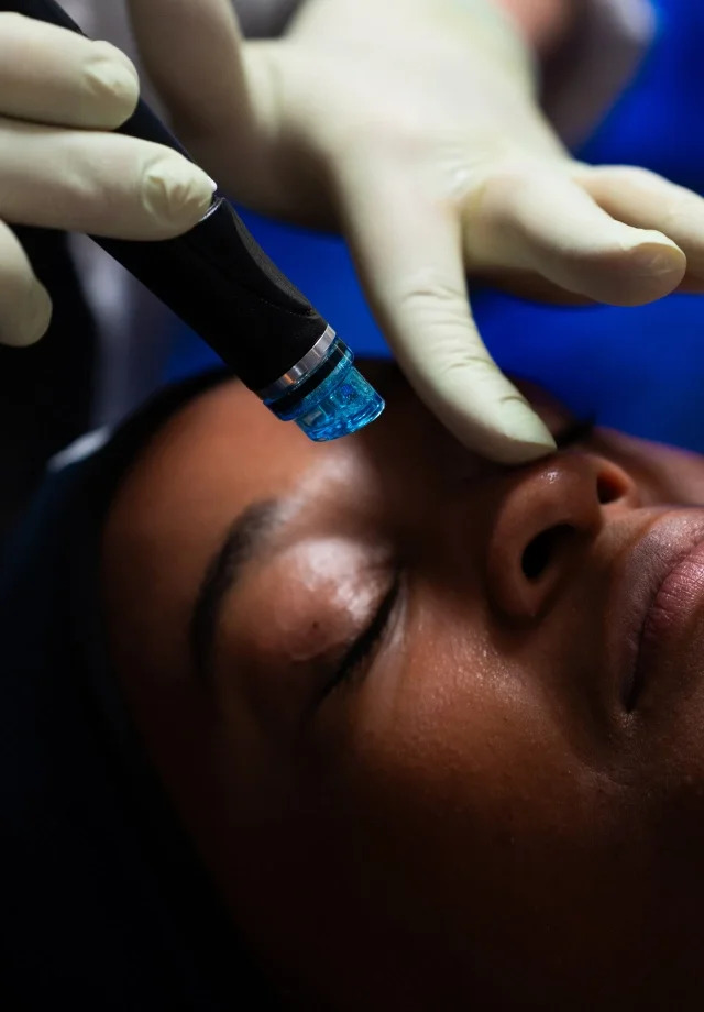 A woman is receiving a facial treatment with a device held above her forehead.