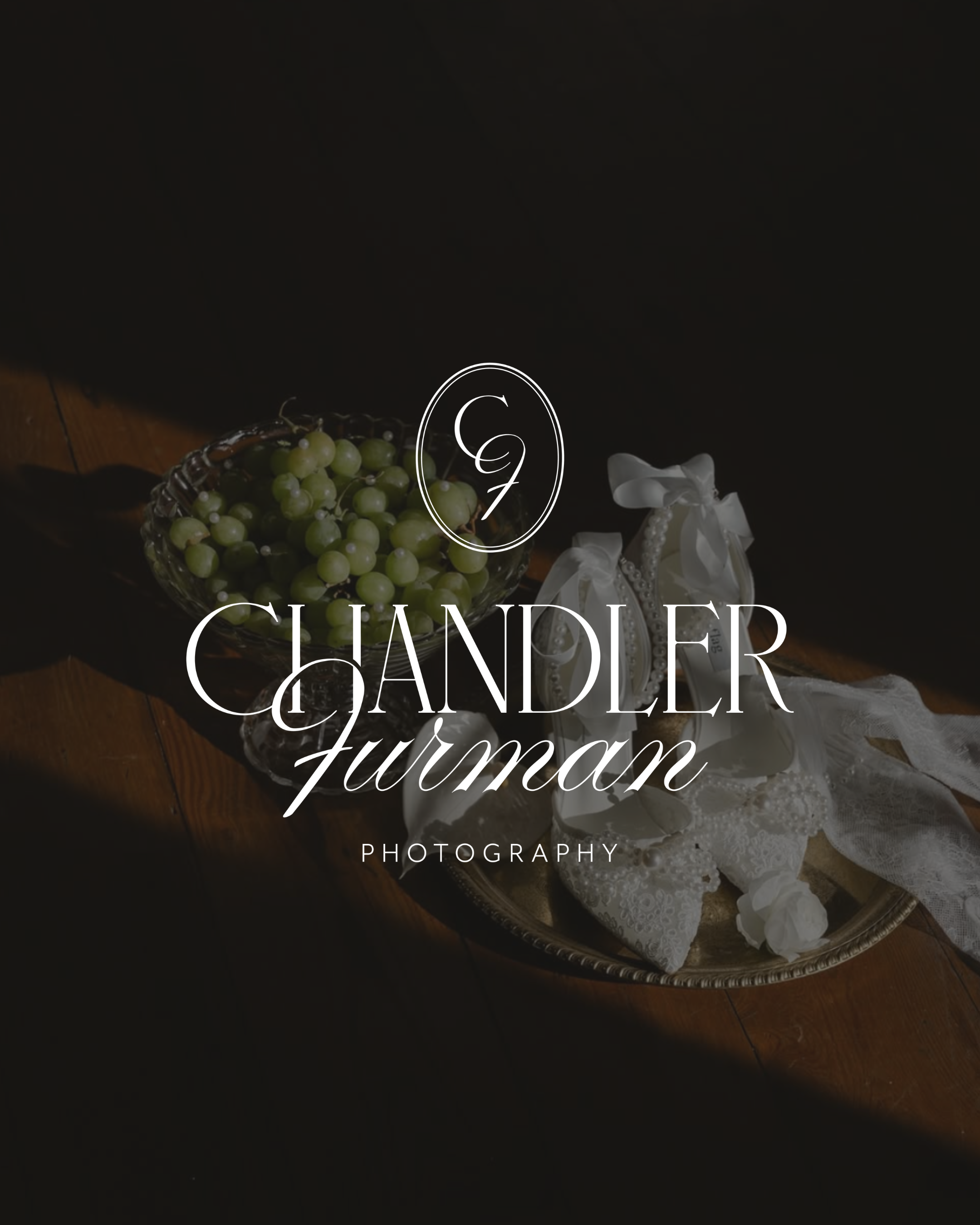 Close-up of a table with a silver tray holding a bunch of green grapes, a white lace cloth, and decorative white ribbons with pearls on a dark background.