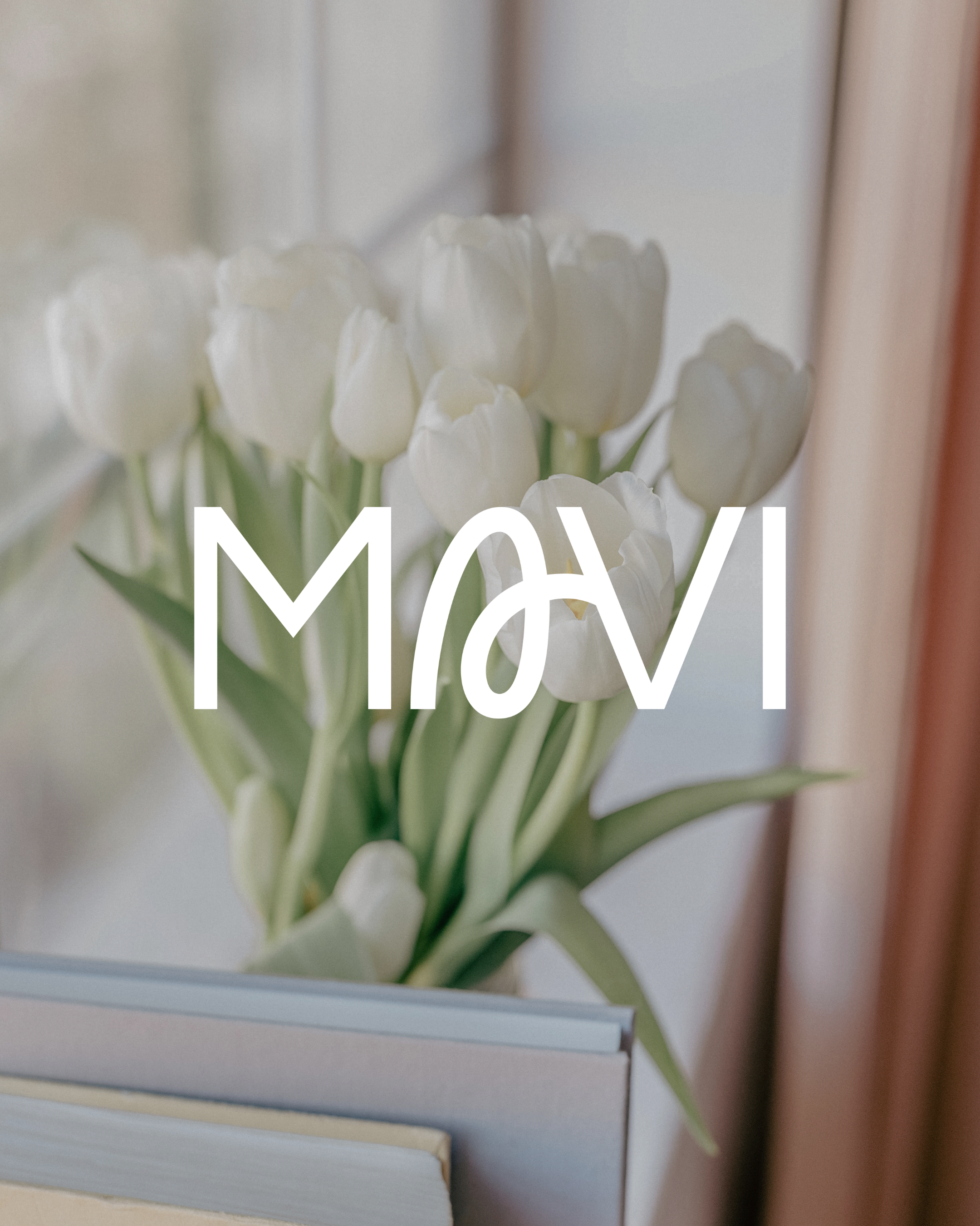 A bouquet of white tulips placed on top of stacked books, with the word 'MAY' overlayed in white text across the image.