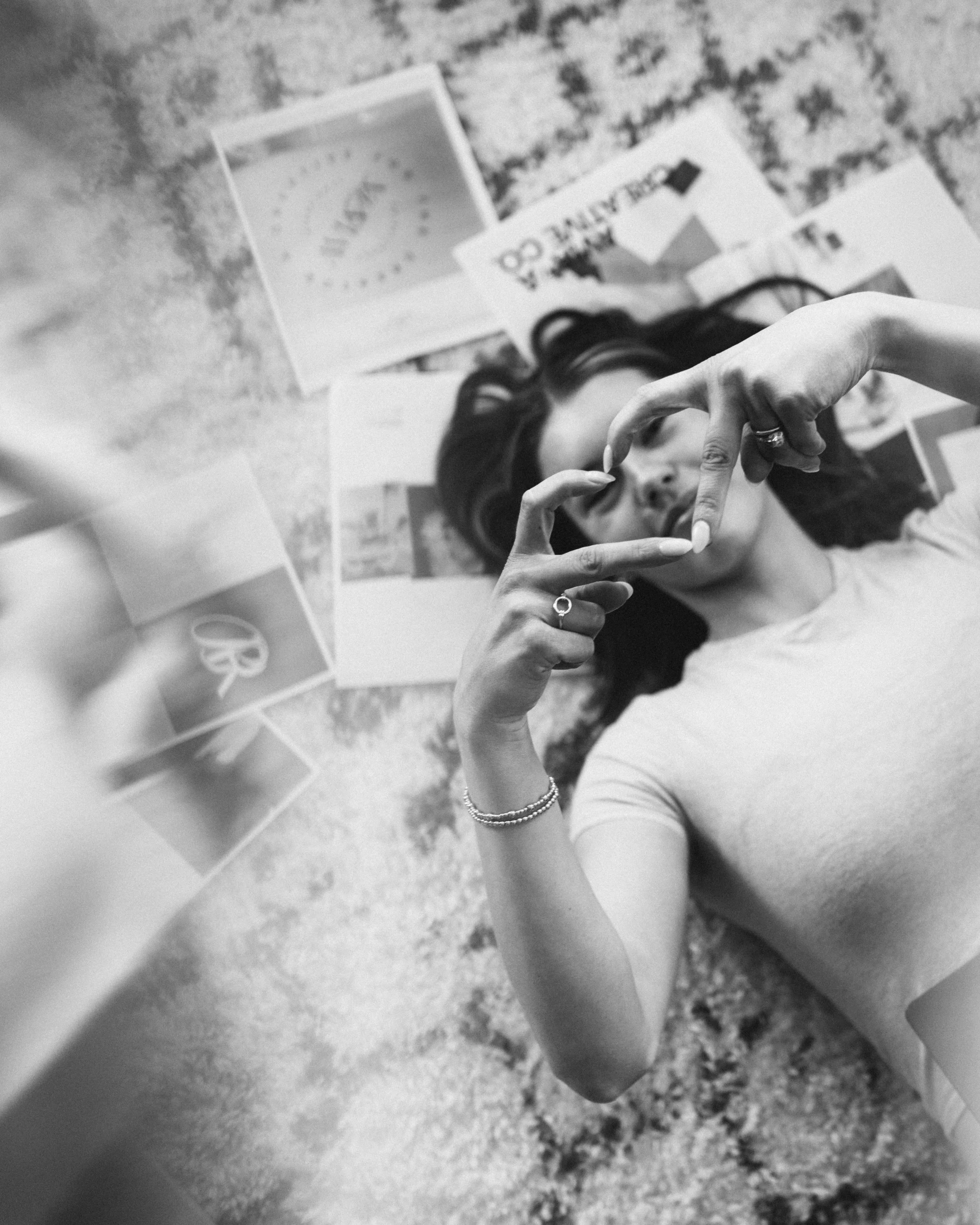A woman with dark hair lying on a patterned carpet, taking a selfie with her phone, with several greeting cards spread out on the floor around her.