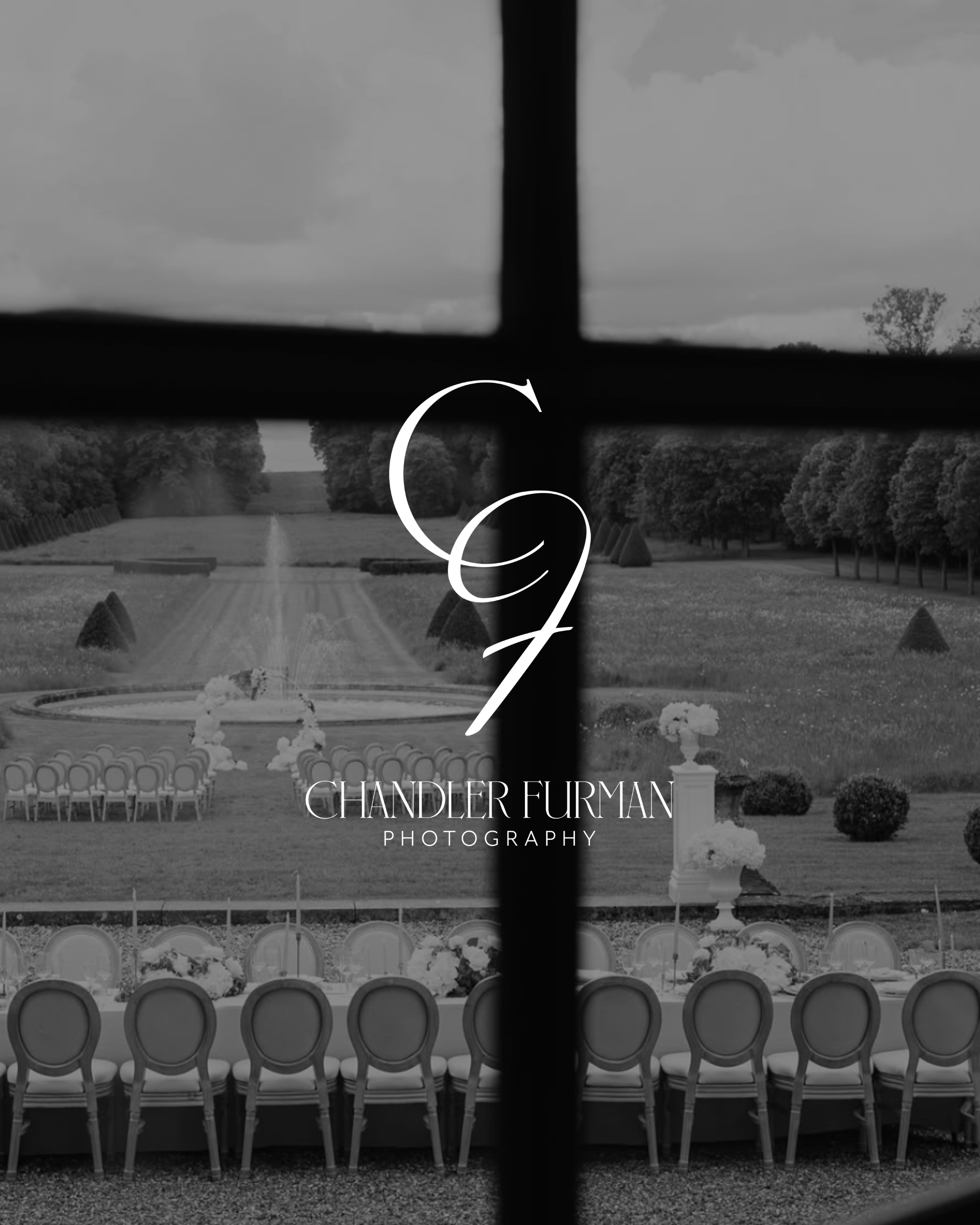 Black and white photo of outdoor wedding setup with rows of chairs facing a decorative aisle and floral arrangements, seen through a window with a cross-shaped bar in the foreground.