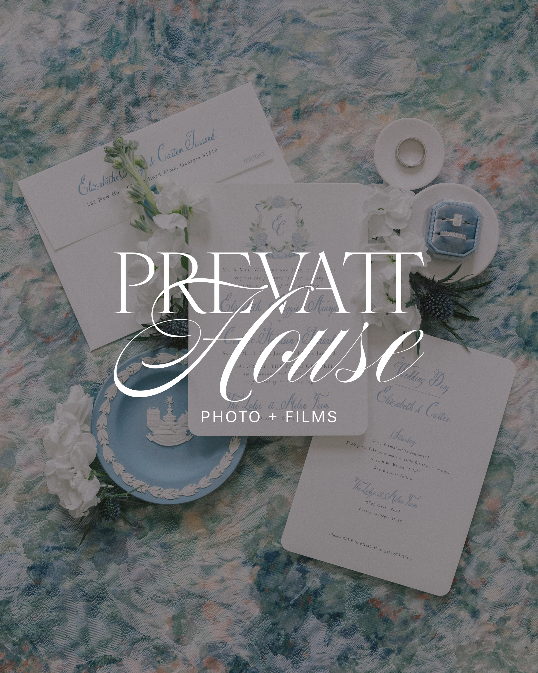 A wedding invitation suite displayed on a floral-patterned fabric. The suite includes a white letterpress invitation, an RSVP card, and additional details, decorated with white flowers and greenery. A ring is placed on a small white dish beside the invitation.