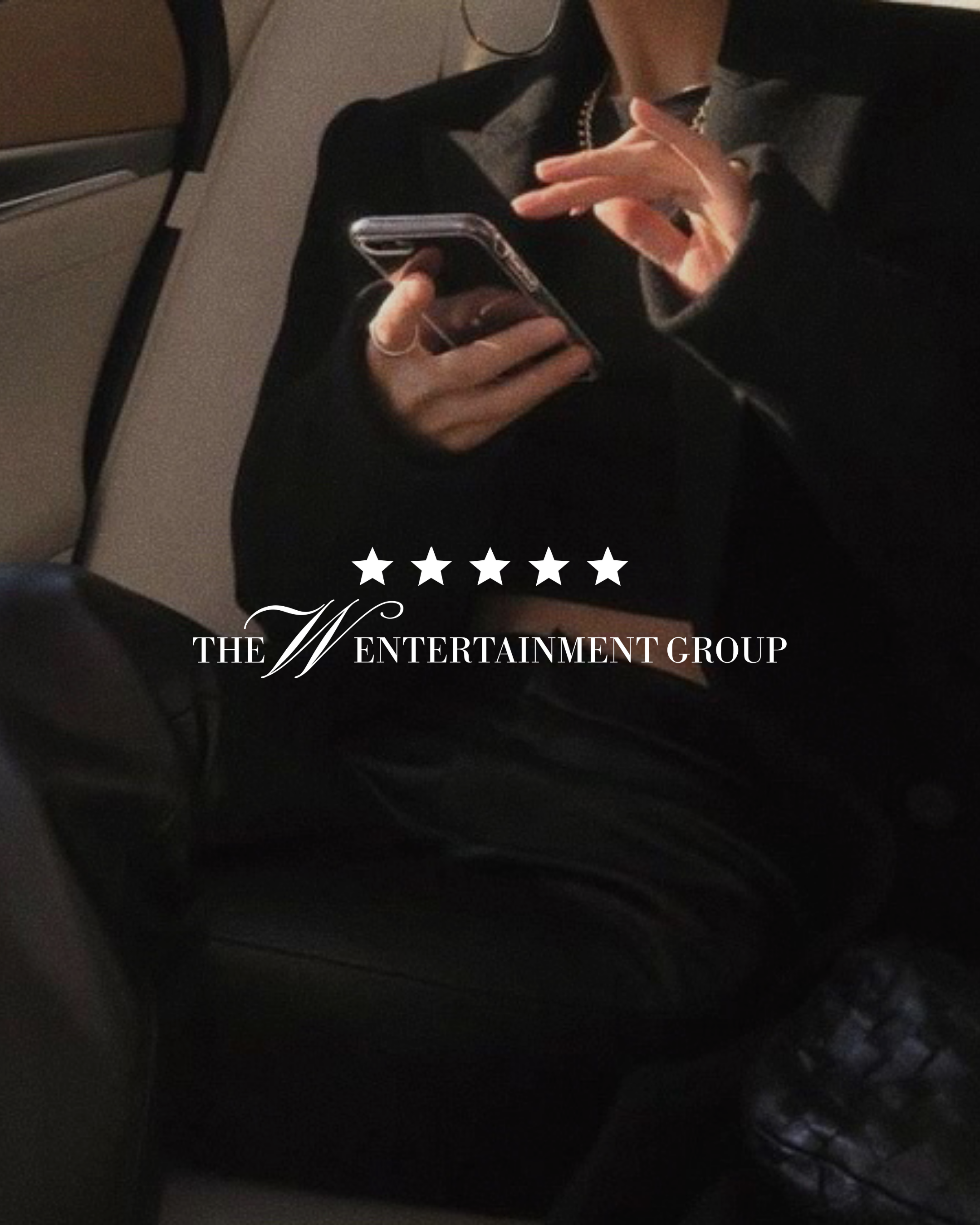 Person holding a smartphone with a case, sitting on a train or bus, wearing a dark jacket and gray shirt, with their hand near their face, and a seat and a small part of the interior in the background.