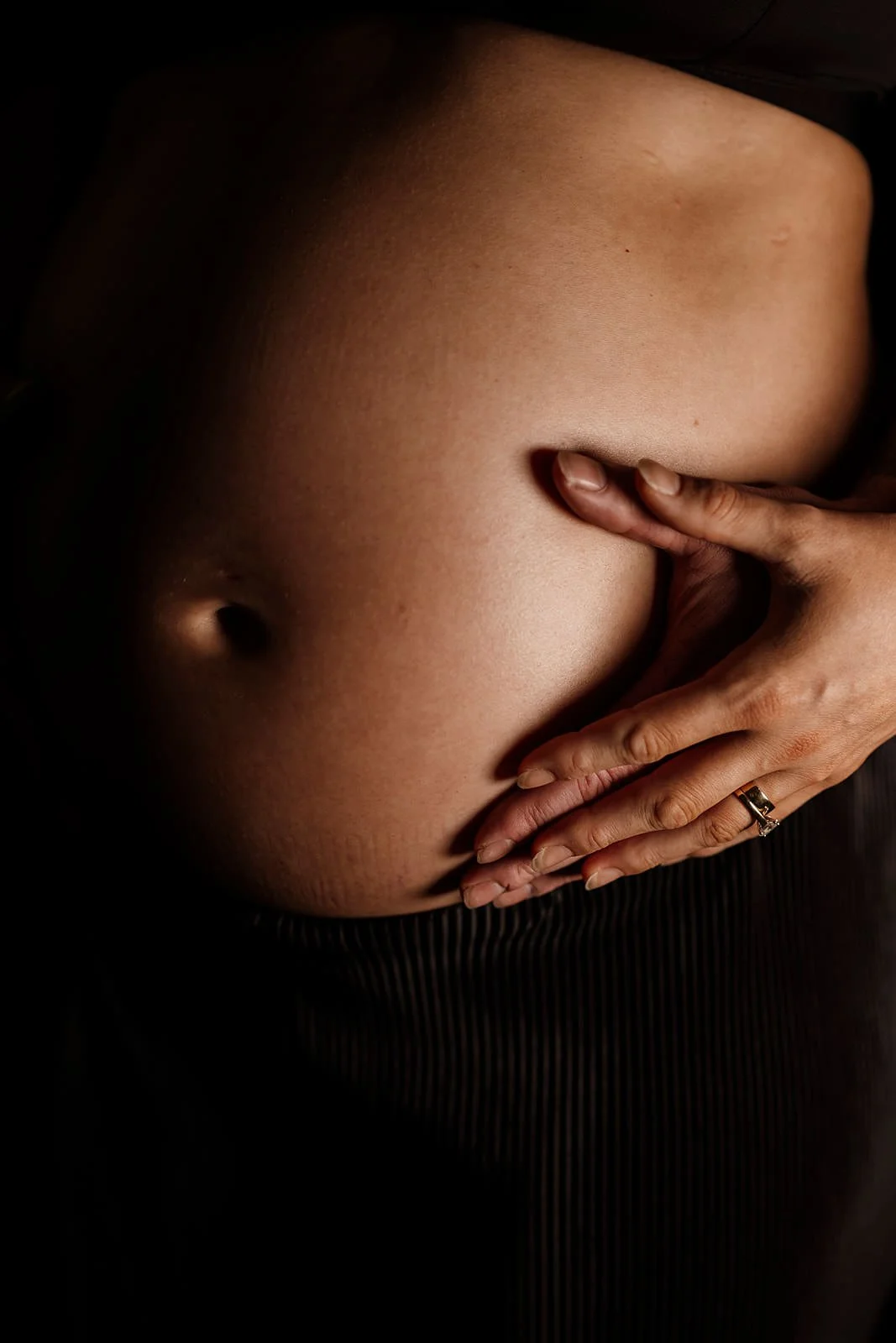 Close-up of a person's bare stomach with a hand gently resting on it, wearing a ring on the finger.