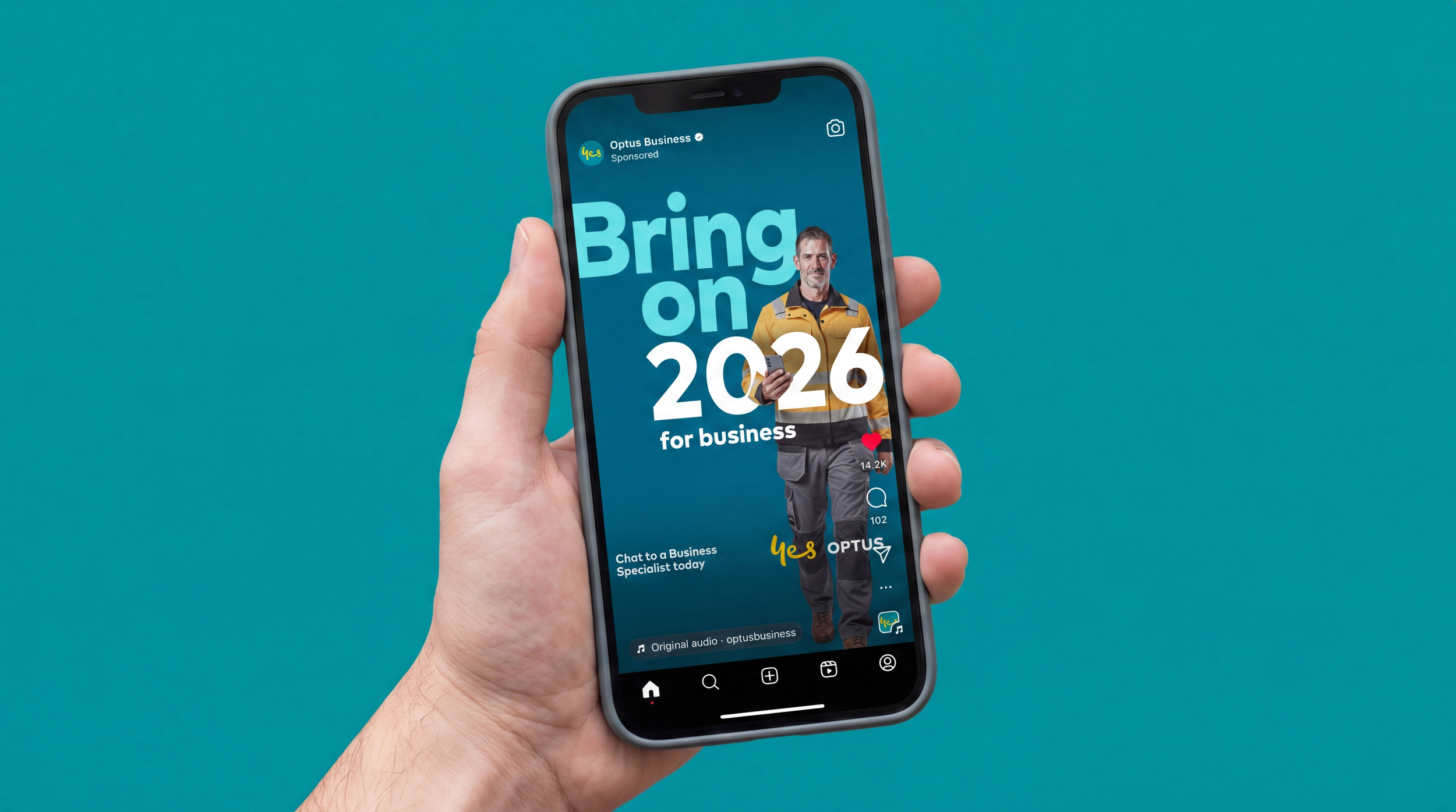 Close-up of a hand holding a smartphone displaying an advertisement for Optus Business with a person in work attire and large text that says 'Bring on 2026' against a teal background.