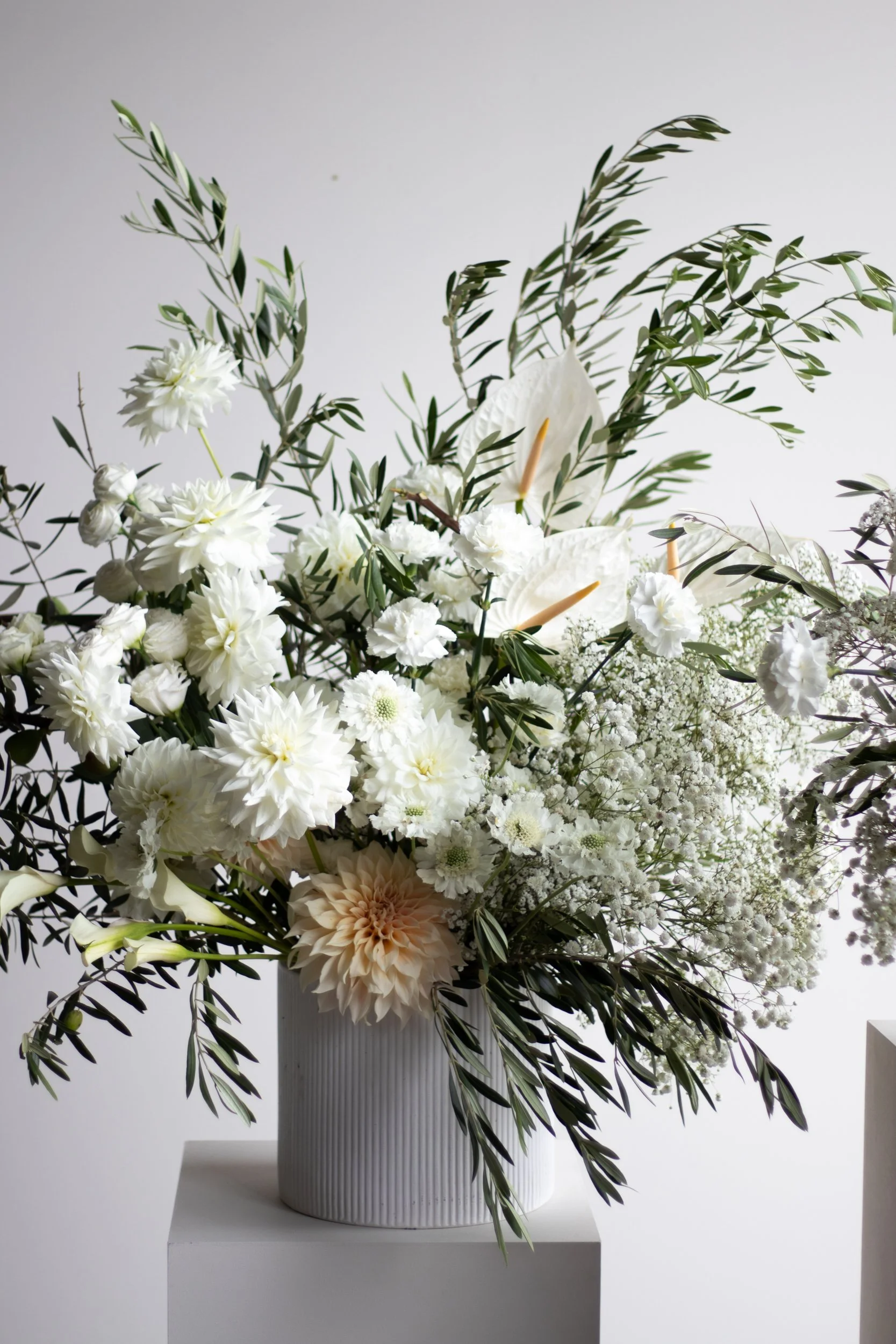 A floral arrangement with white flowers like dahlias and anthuriums in a white vase, set on a pedestal.