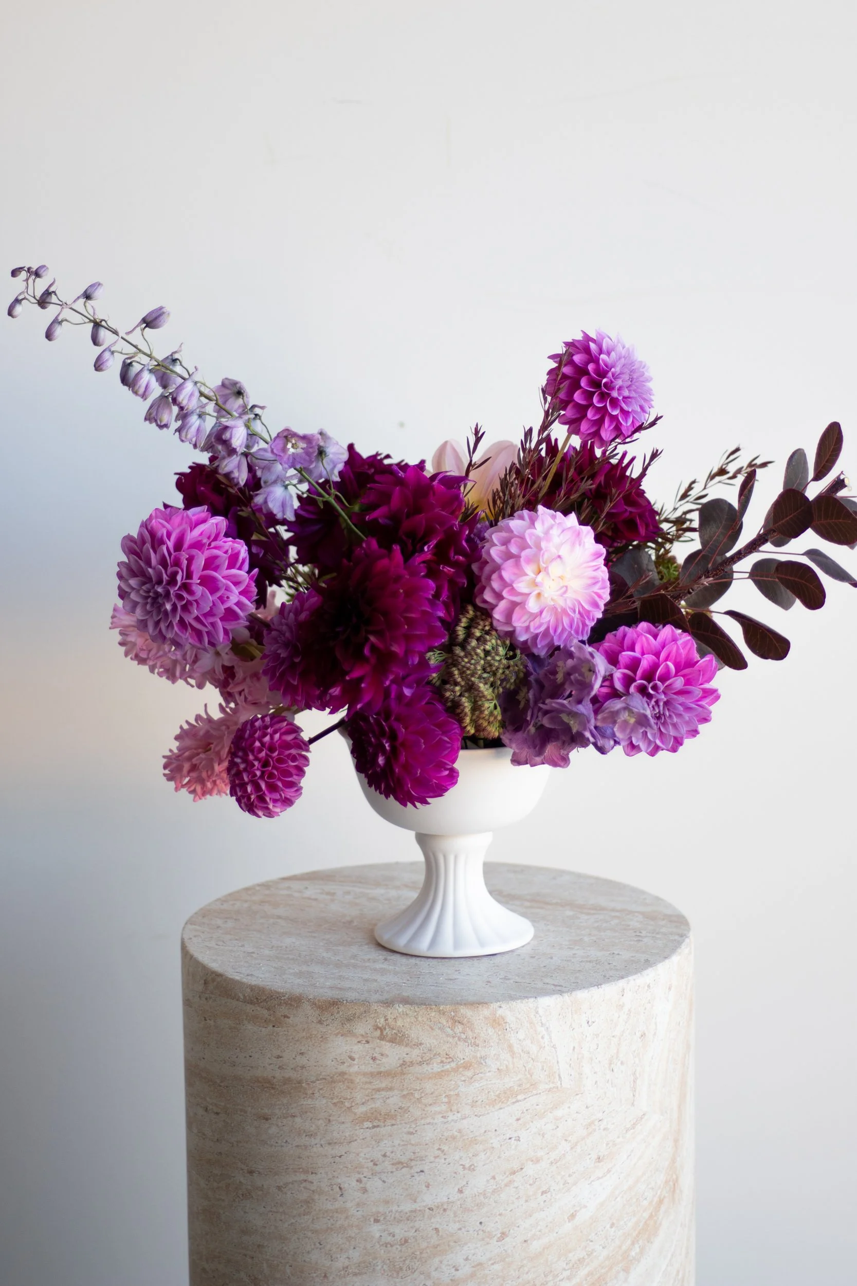 Elegant floral arrangement with purple and pink flowers in a white vase on a stone pedestal.
