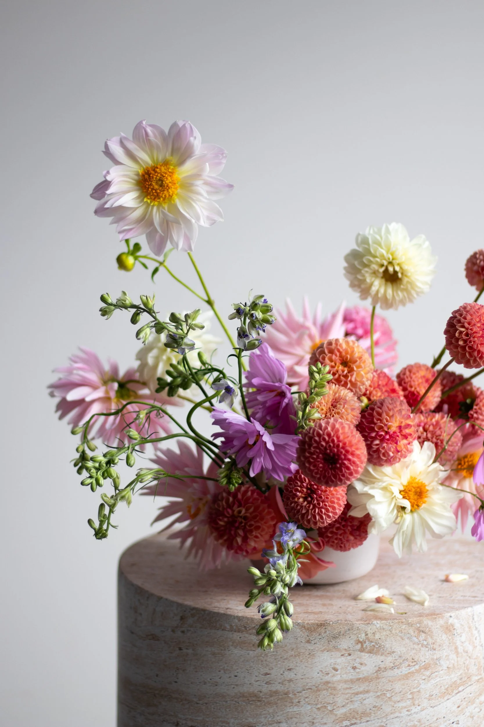 Colorful flower arrangement featuring white, pink, and red dahlias, and other assorted flowers on a stone pedestal.