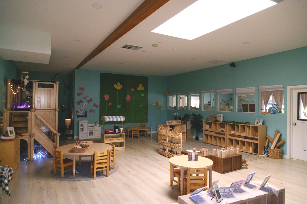 Empty daycare space with wooden furniture, storage shelves, and a wall decorated with flowers and butterflies.