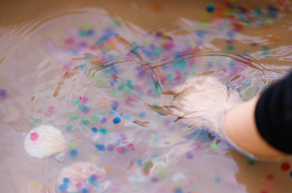 A child's hand stirring colorful confetti in water.