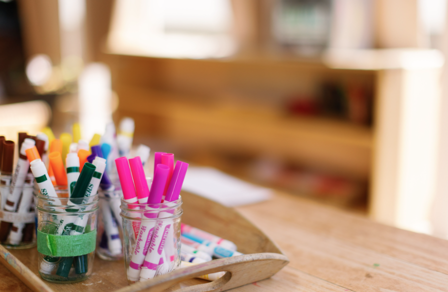 Assorted colorful markers in glass jars on a wooden surface.