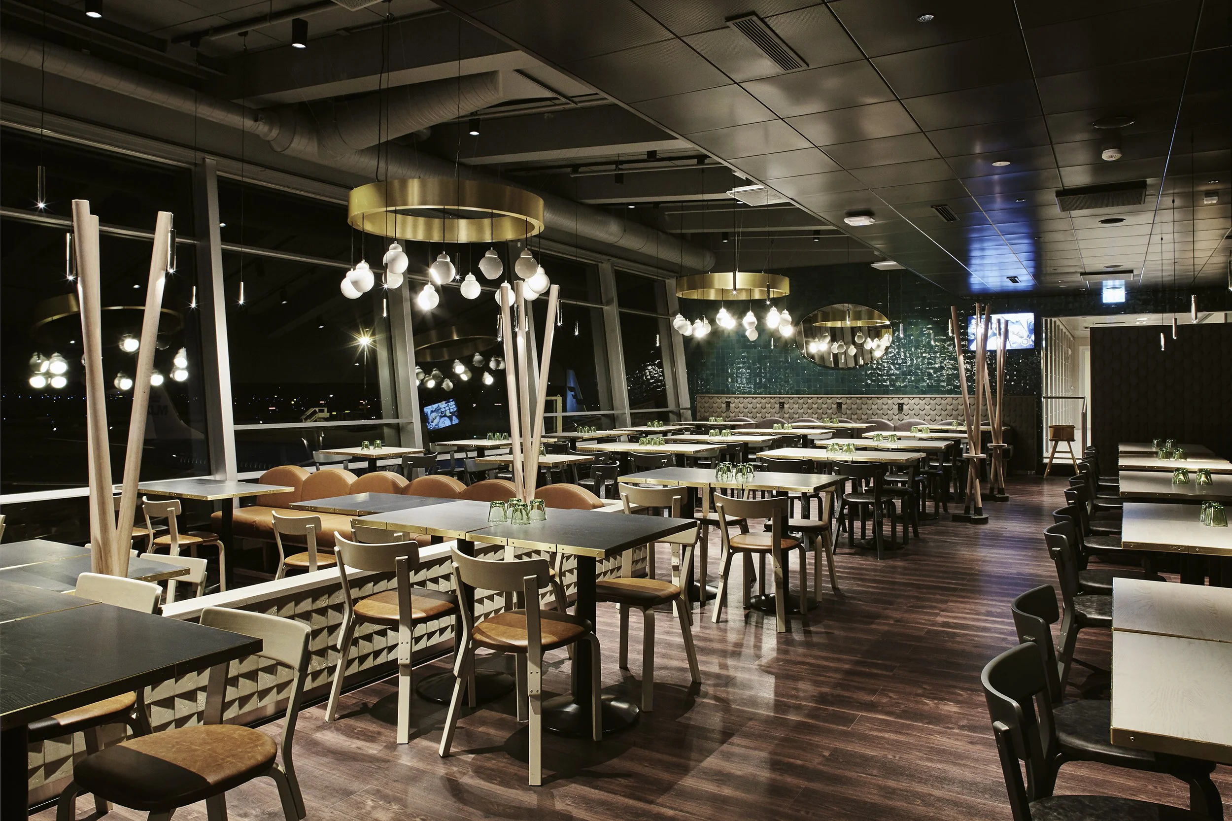 Tyhjä ravintolasali illalla, moderneja pöytiä ja tuoleja, kelloja ja seinäkoristeita, säteitä ja peilejä, ikkunat, hiljainen ja elegantti tunnelma.