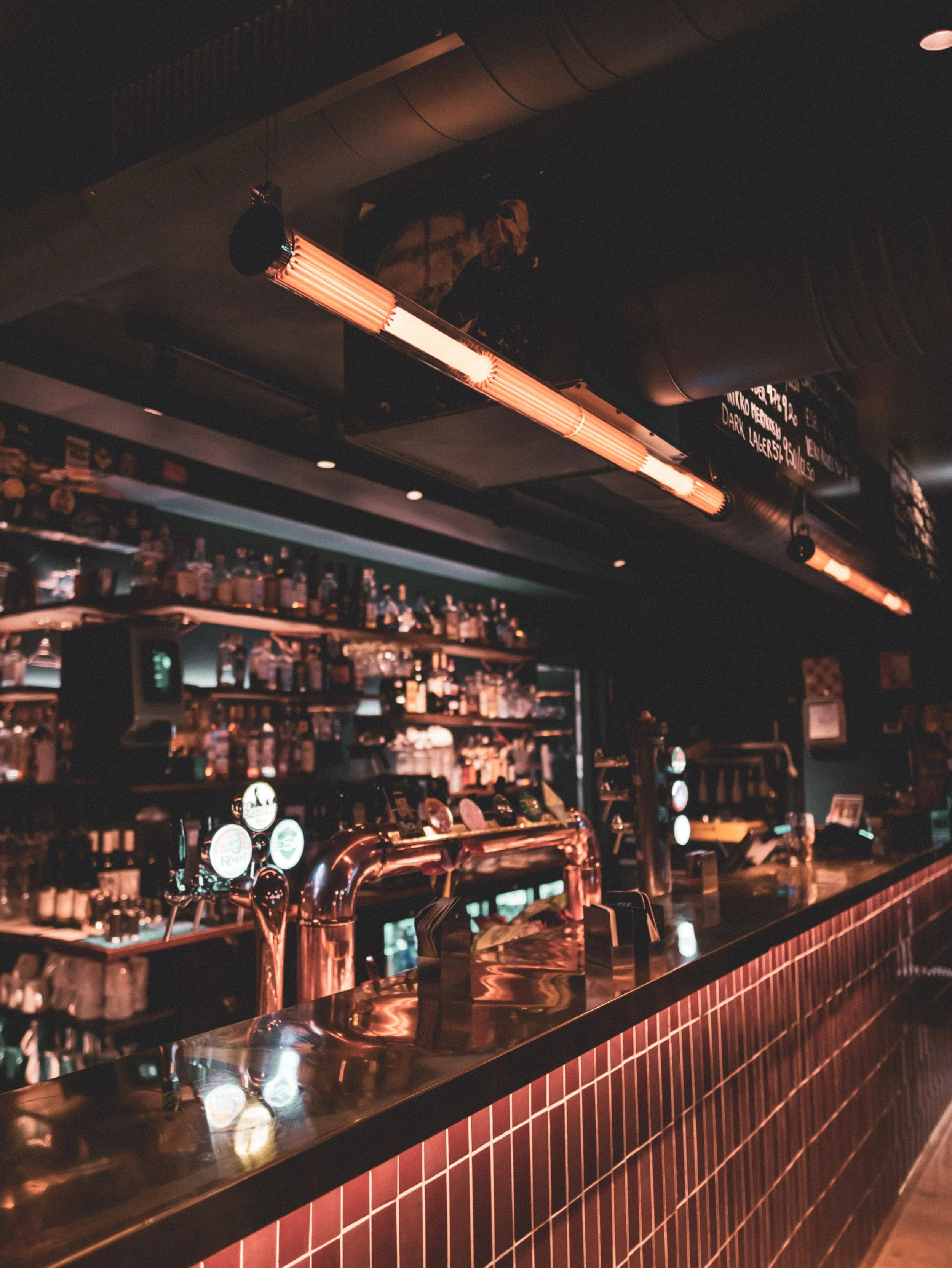 Hauki punaisessa valaistuksessa oleva baaritiski, taustalla hylly täynnä alkoholijuomia, katto ja seinät tummat.