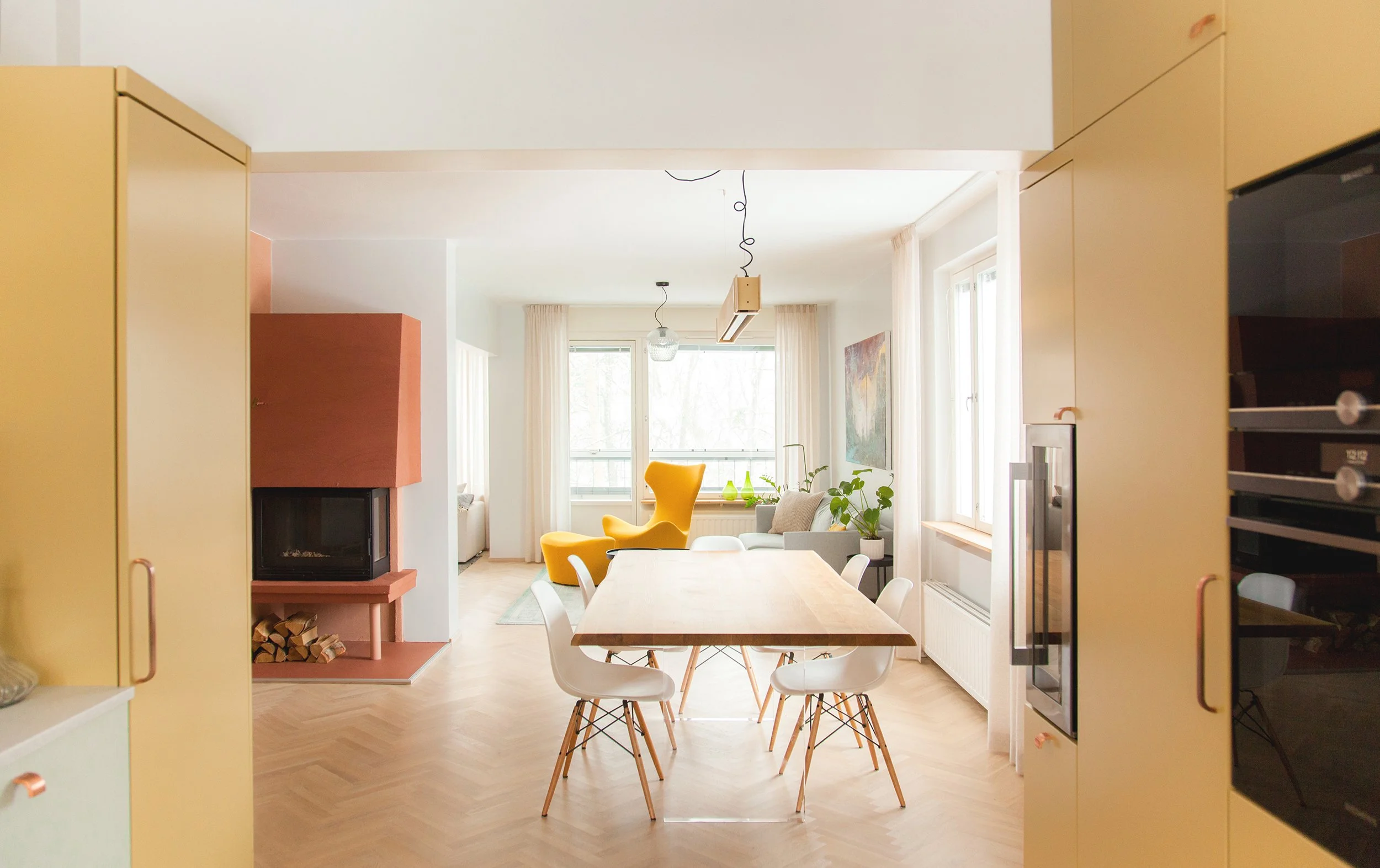 Valoisa ravintolapöytä ja tuolit, olohuone ja takka ikkunasta katsottuna.