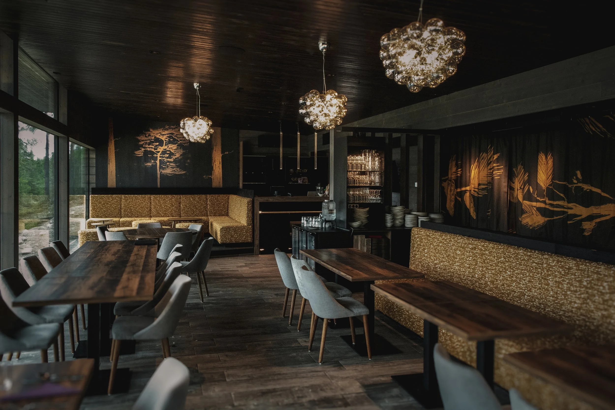 Modernin ravintolan sisätila pehmeillä valaisimilla ja suurella ikkunalla, jossa näkee ulos luontoa.