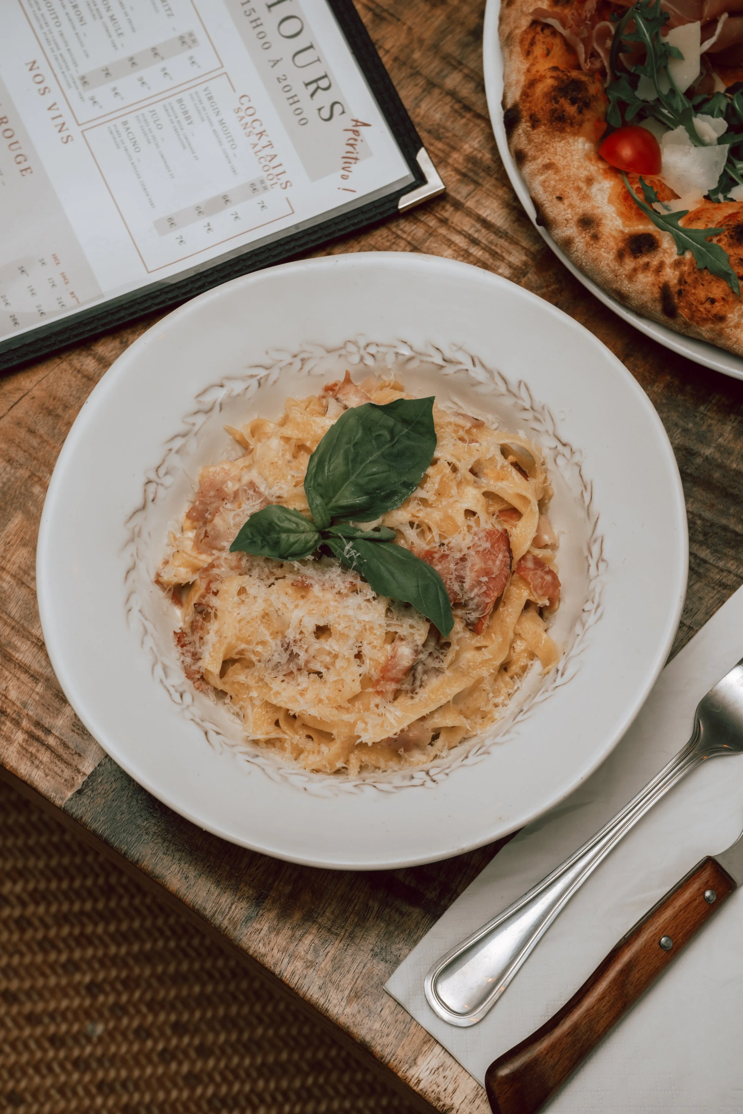 Plat de pâtes à la crème garnie de parmesan et basilic, avec une pizza à côté