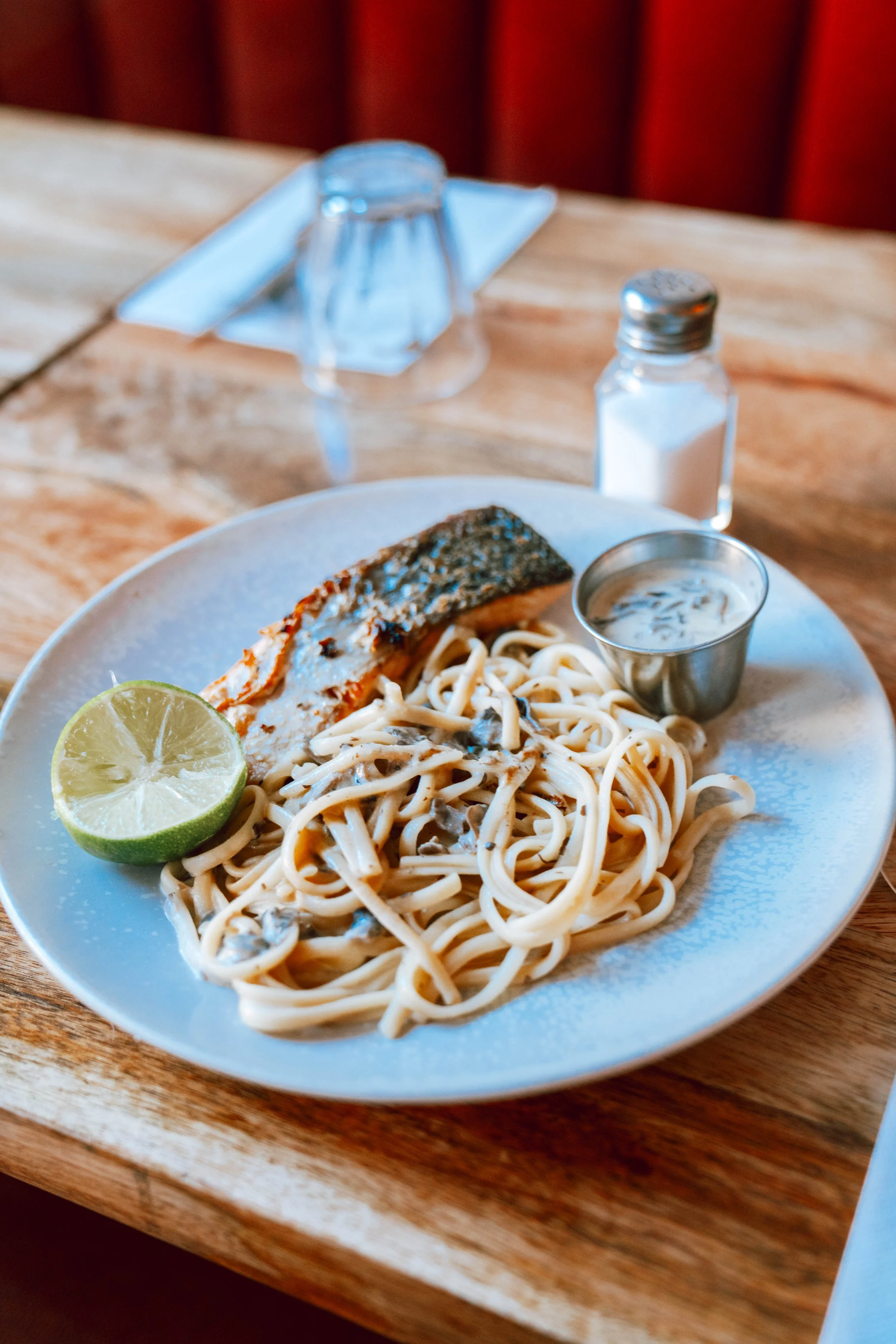 Assiette de pâtes avec saumon, citron vert, sauce crémeuse aux champignons, et une bouteille de sel sur une table en bois.