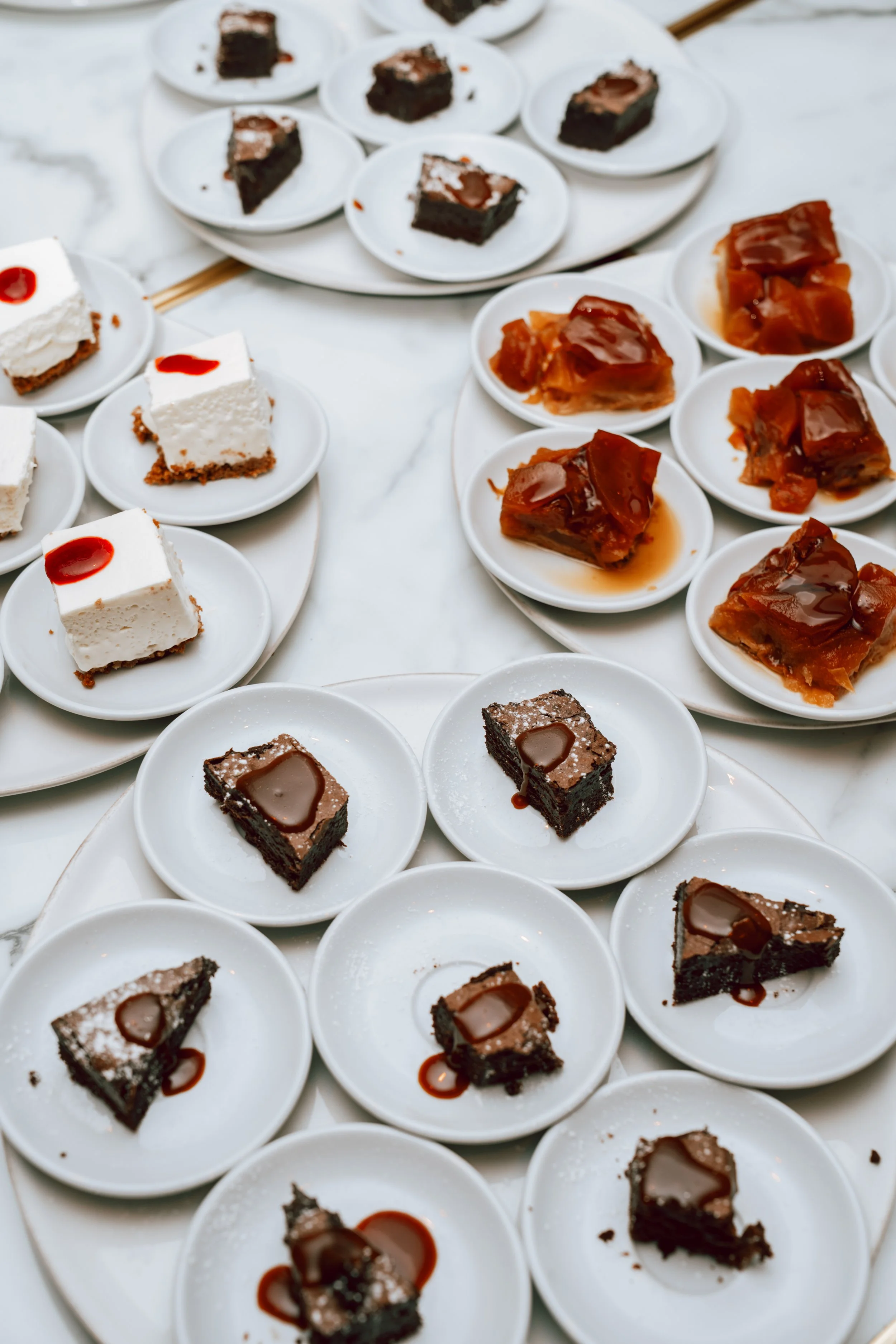 Assortiment de petits desserts sur des assiettes blanches, comprenant des parts de gâteau au chocolat, cheesecake, et tarte aux fruits.