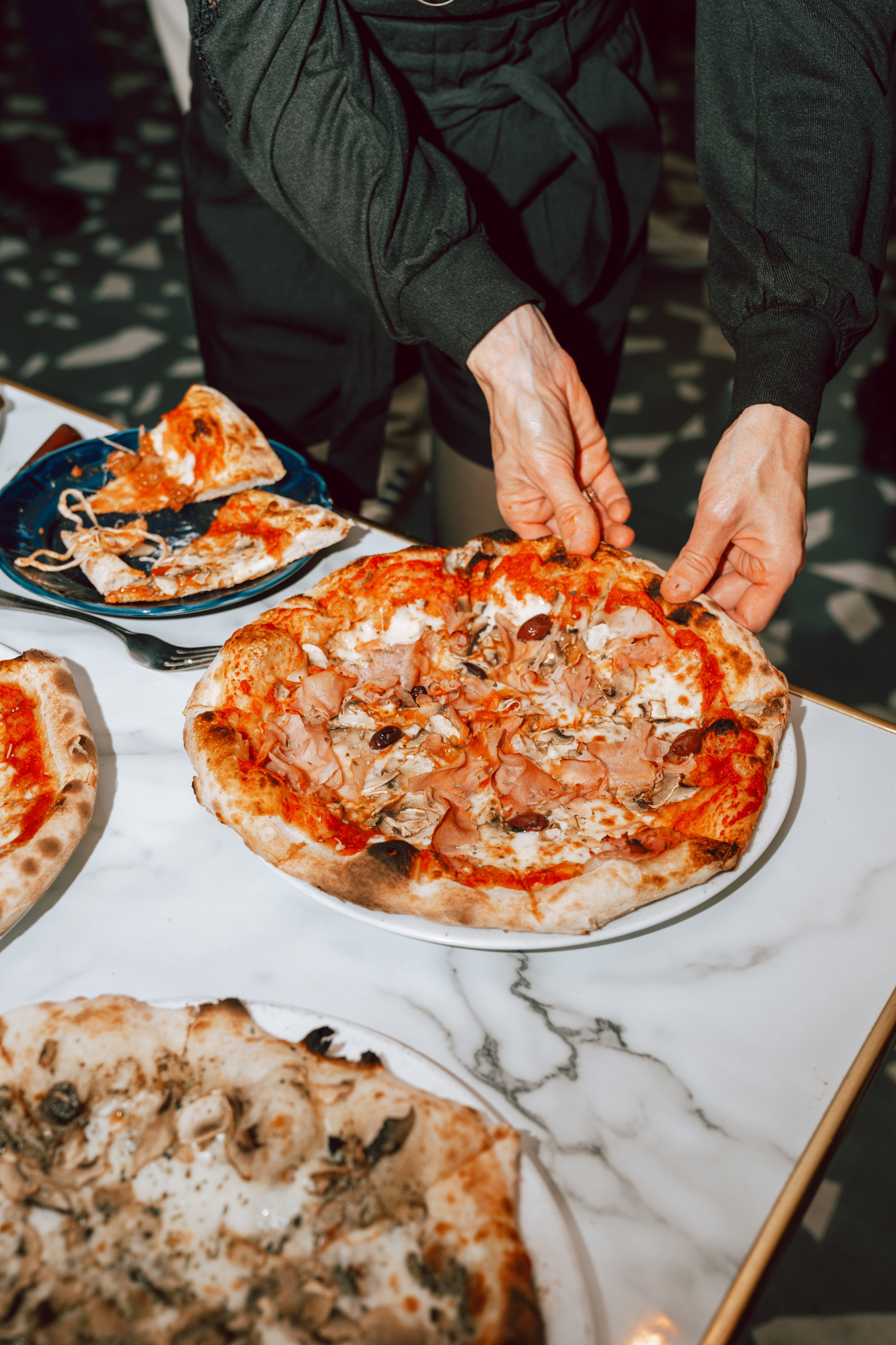 Person servant une pizza avec des champignons, jambon et olives sur une table en marbre