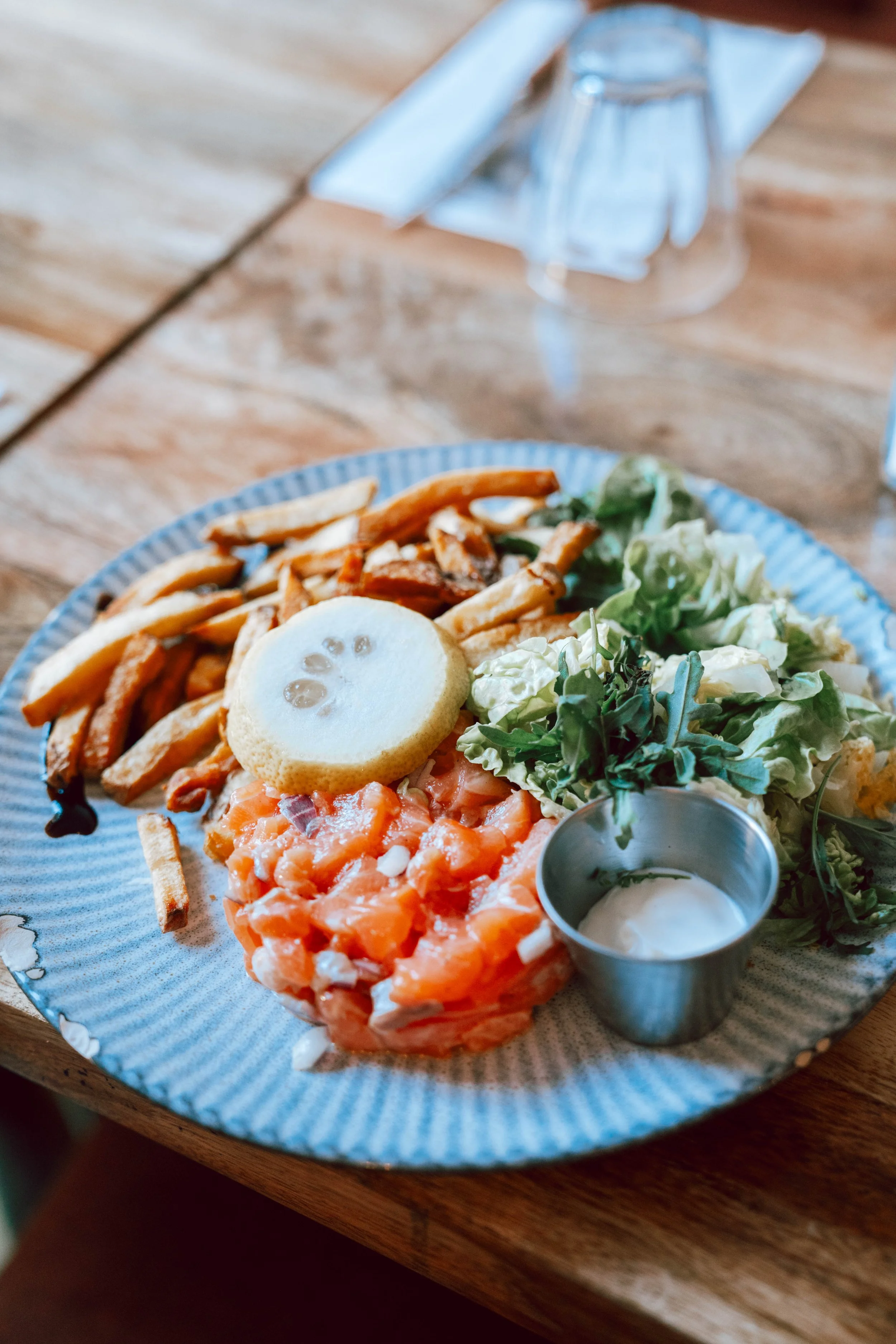 Assiette de saumon fumé avec salade, frites, œuf de caille, sauce et citron, sur une table en bois