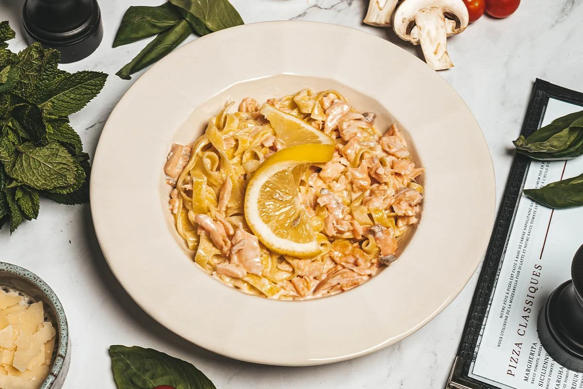 Pâtes aux morceaux de saumon, sauce à la crème, avec tranche de citron à dessus, dans une assiette blanche
