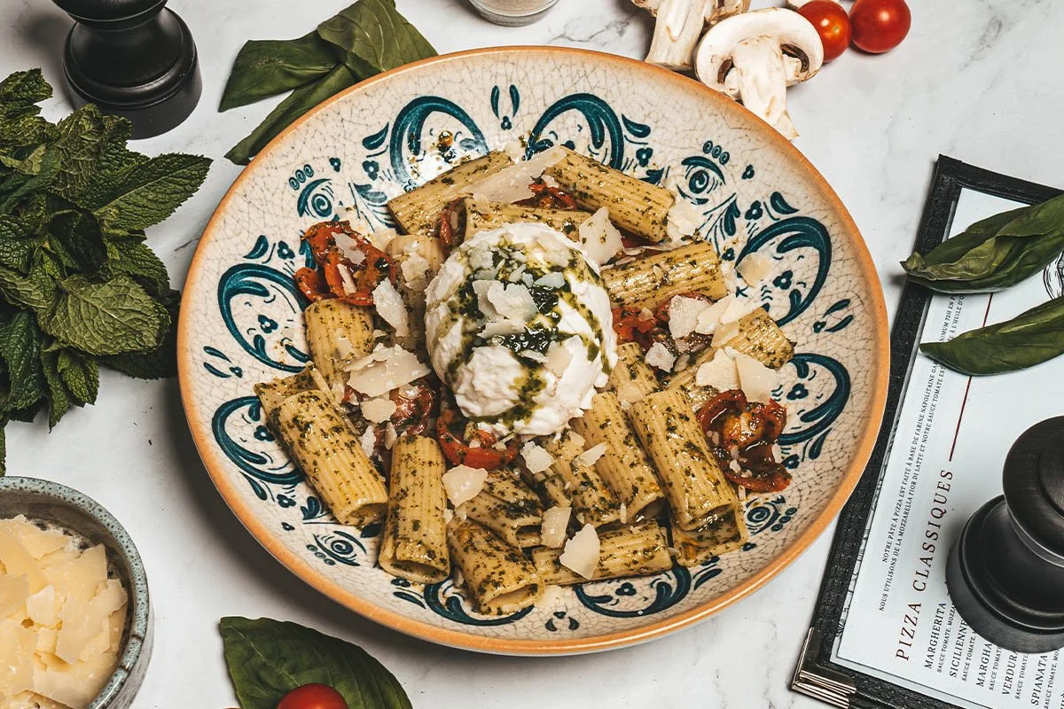 Assiette de pâtes rigatoni avec sauce, tomate, basilic, mozzarella, parmesan, et huile d'olive. Accompagnée de tomates cerises, champignons, basilic frais, et fromage.
