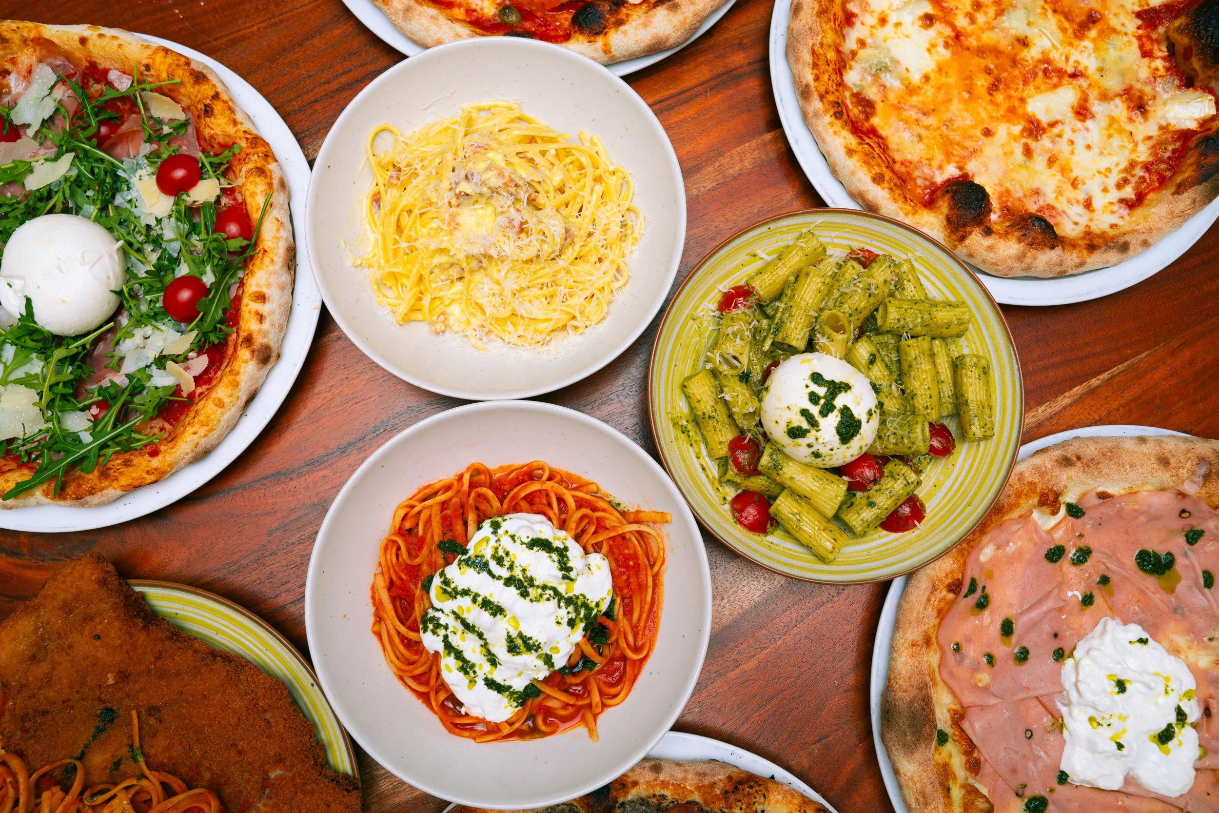 Assortiment de pizzas, pâtes et salades sur une table en bois.