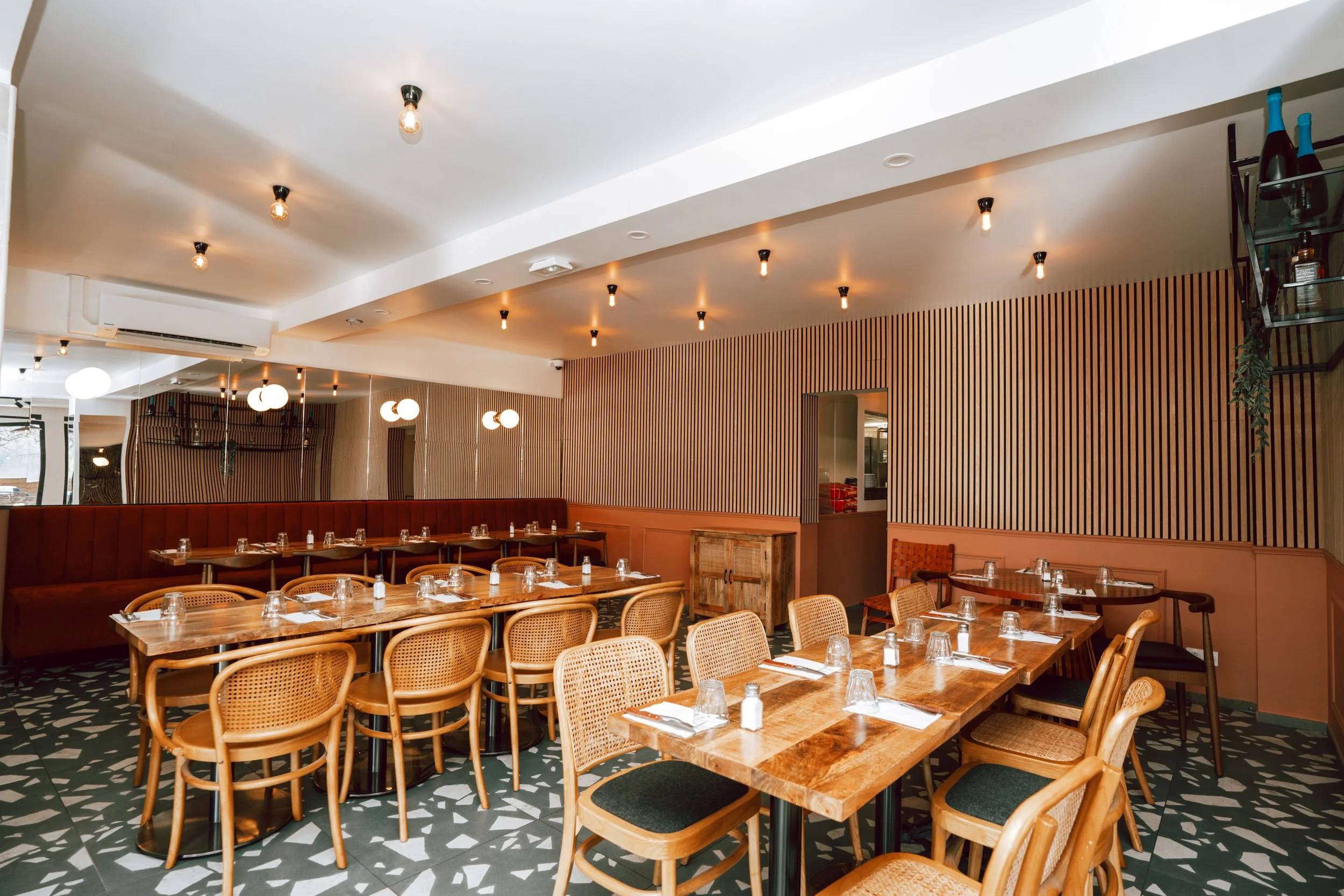 Salle à manger d'un restaurant avec des tables en bois, des chaises en osier et des verres sur les tables, mur en bois vertical et éclairage plafond