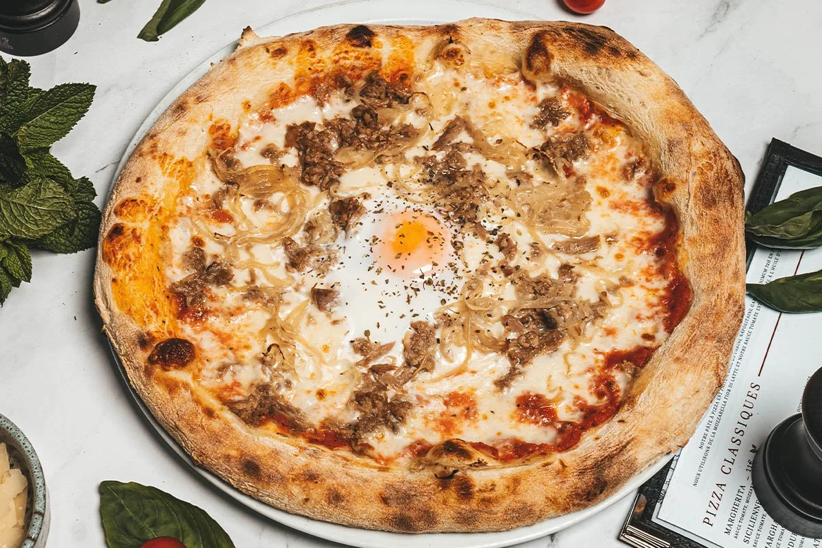 Pizza with cheese, ground meat, onions, and a fried egg in the center, on a white plate.