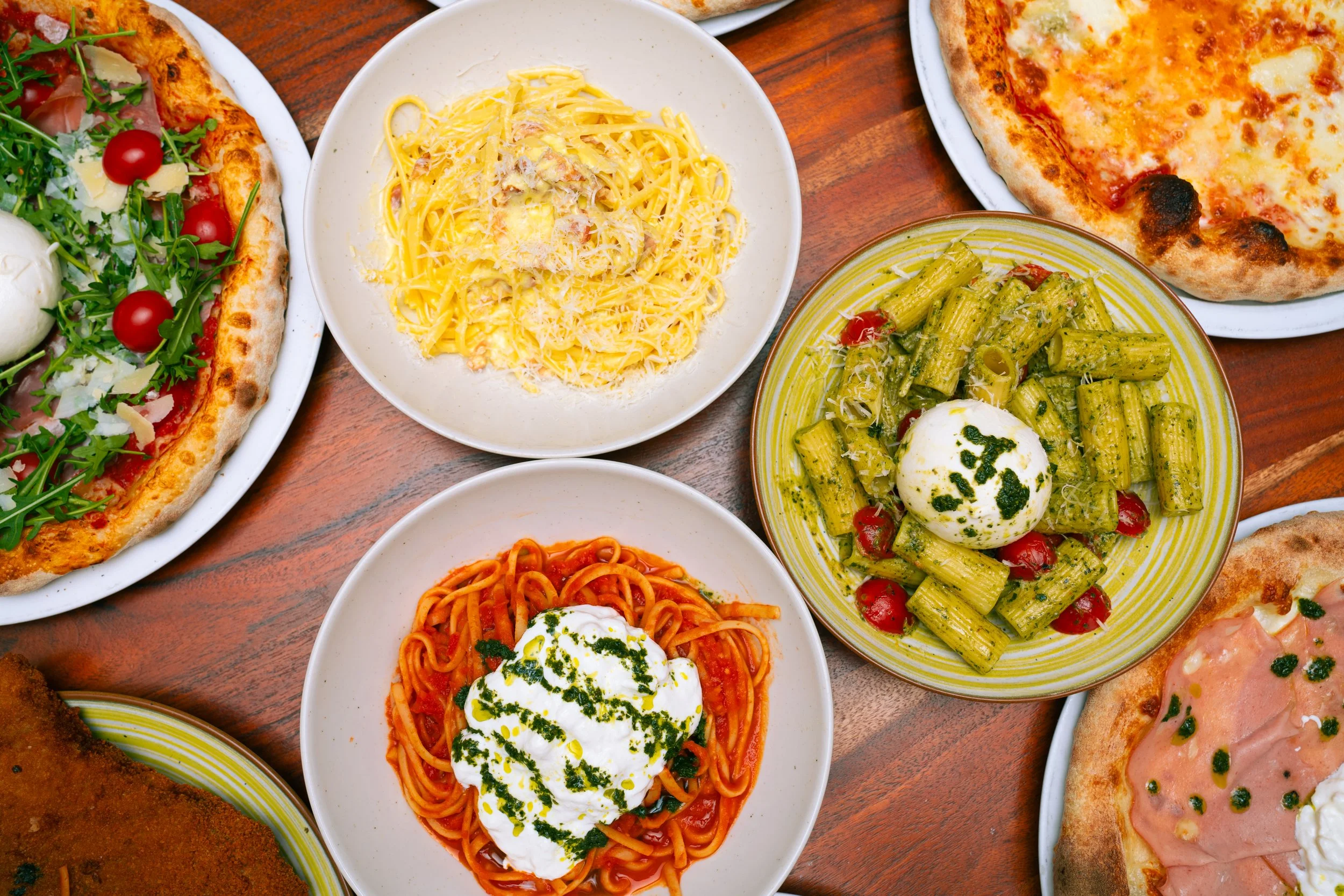 Divers plats de pizza, pâtes, et salade sur une table en bois.